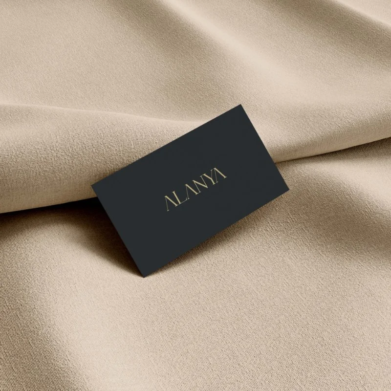 Close-up of a beige fabric surface with a black business card that has gold text reading 'ALANYA' resting on it.