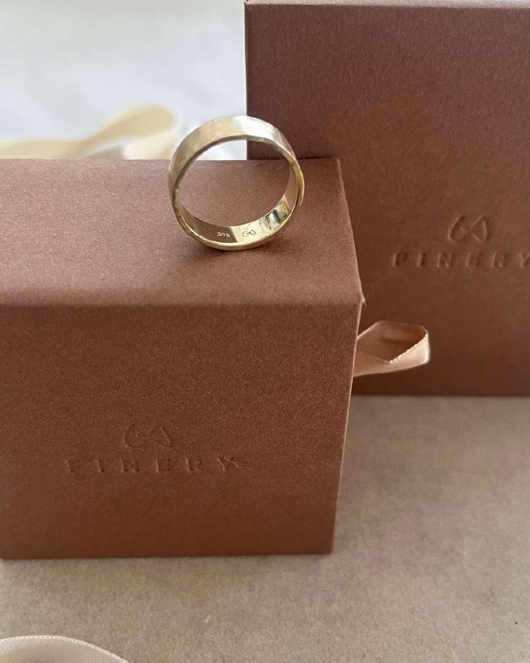 Silver ring placed on a brown jewellery box with 'L.A. Finery' embossed, next to a matching pink box with a ribbon.