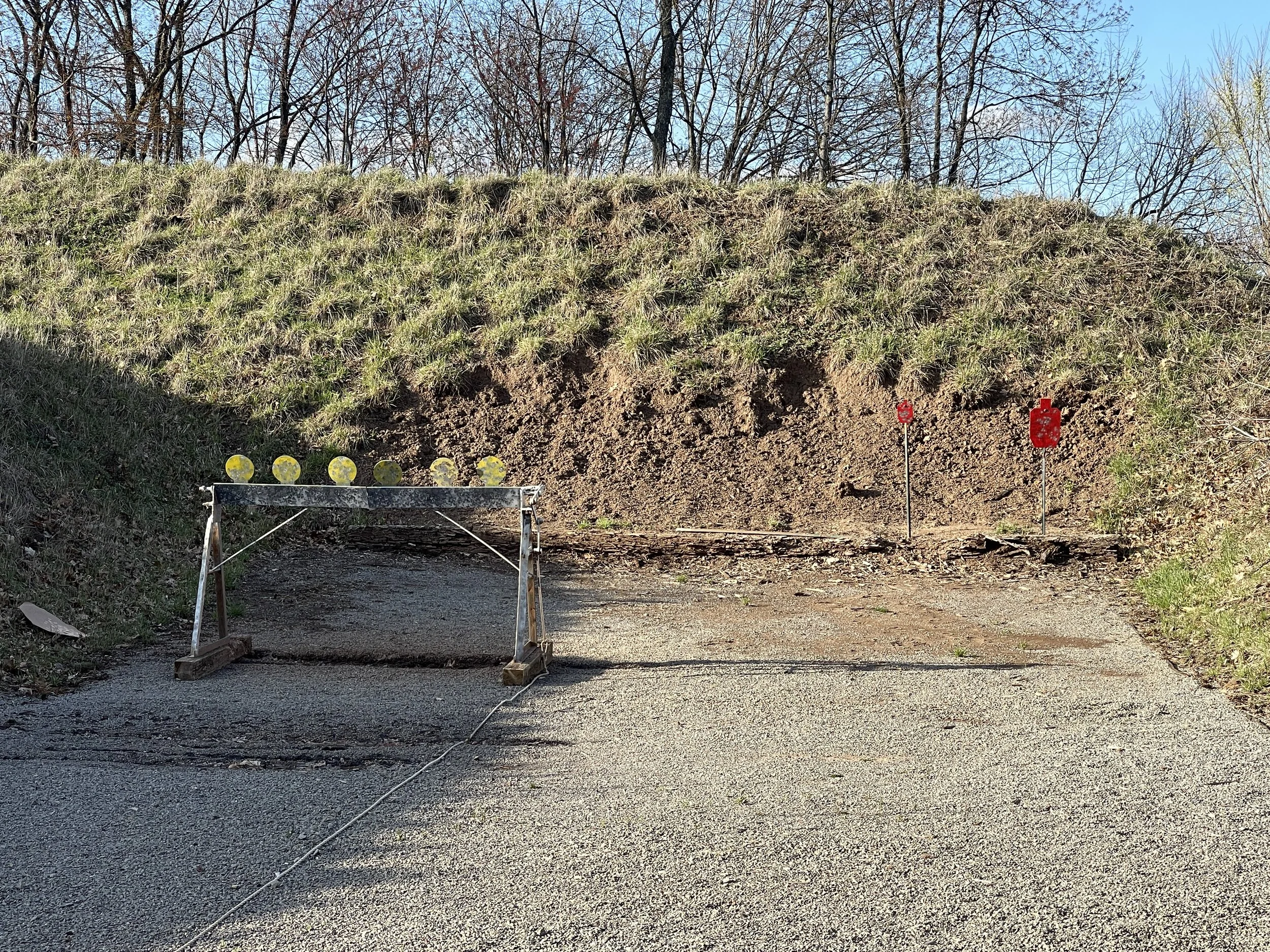 Construction site blocking off a section of road with warning signs, a barricade, and a slope with grass and trees in the background.