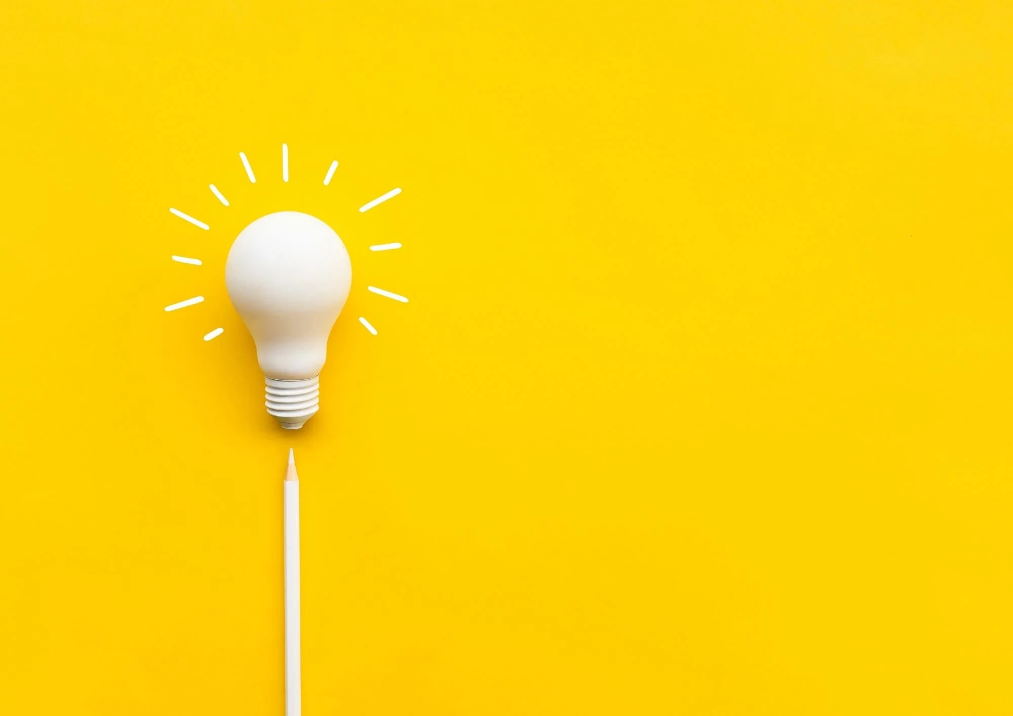 A white light bulb with lines drawn around it, representing an idea, on a yellow background with a pencil beneath it.