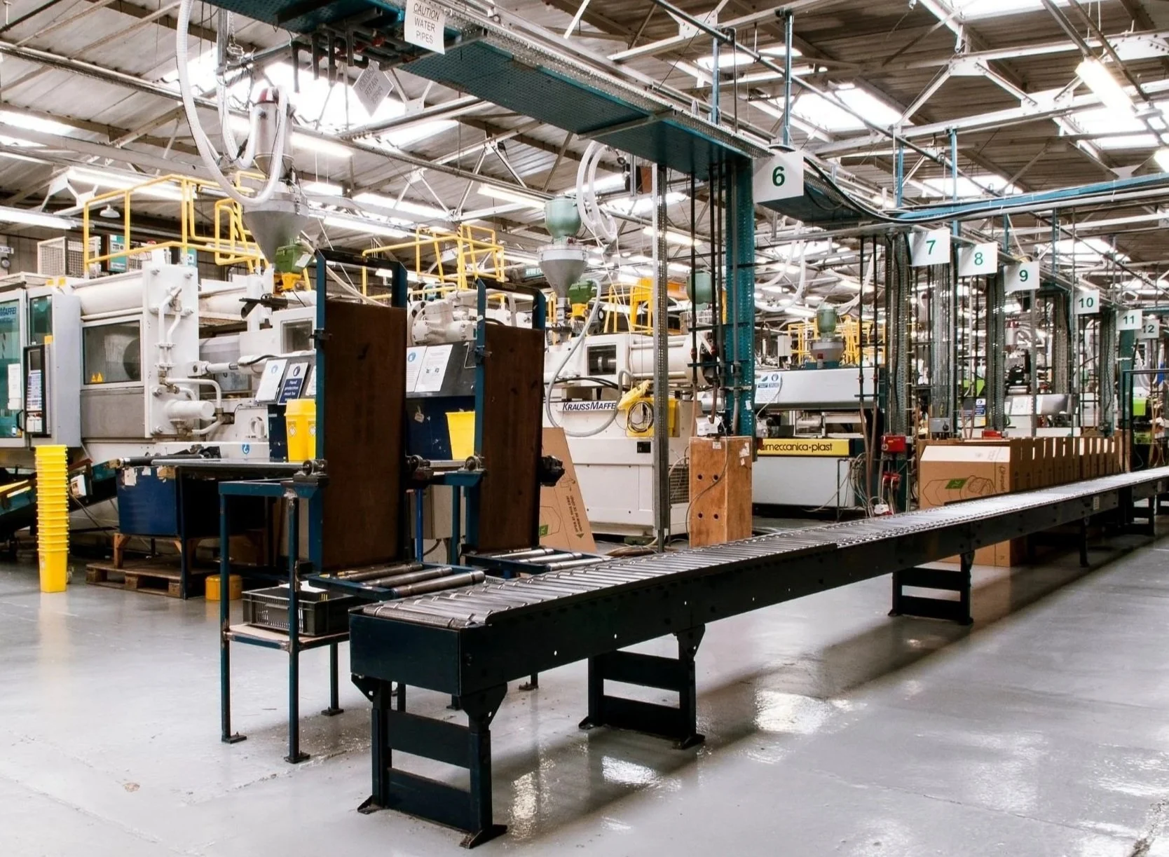 Industrial manufacturing facility with machinery, conveyor belts, and equipment for processing or packaging materials. The space is brightly lit with a high ceiling and labeled sections.