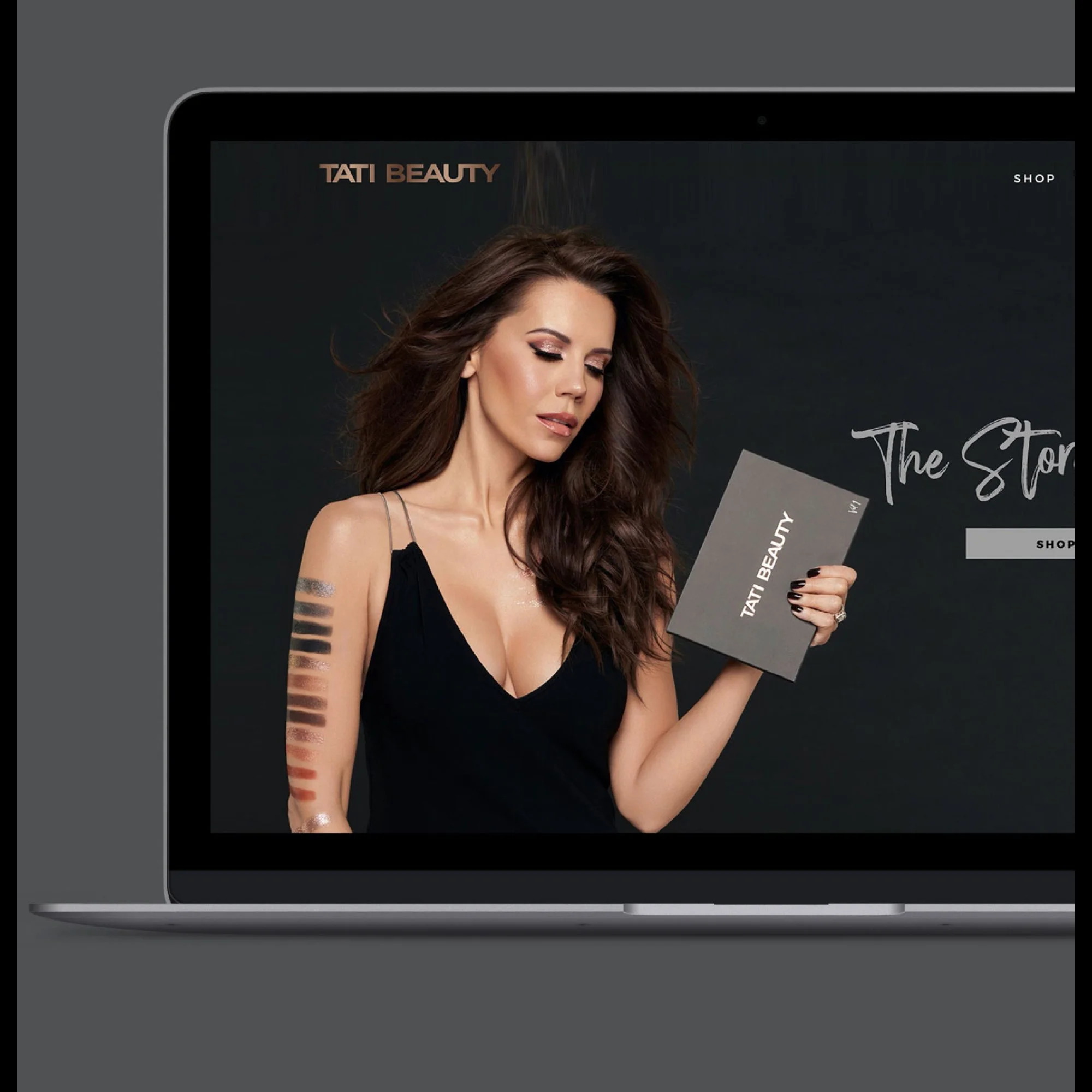 Laptop displaying an online beauty store called Tati Beauty, featuring a woman with long brown hair, makeup, and a black spaghetti strap top, holding a makeup catalog.