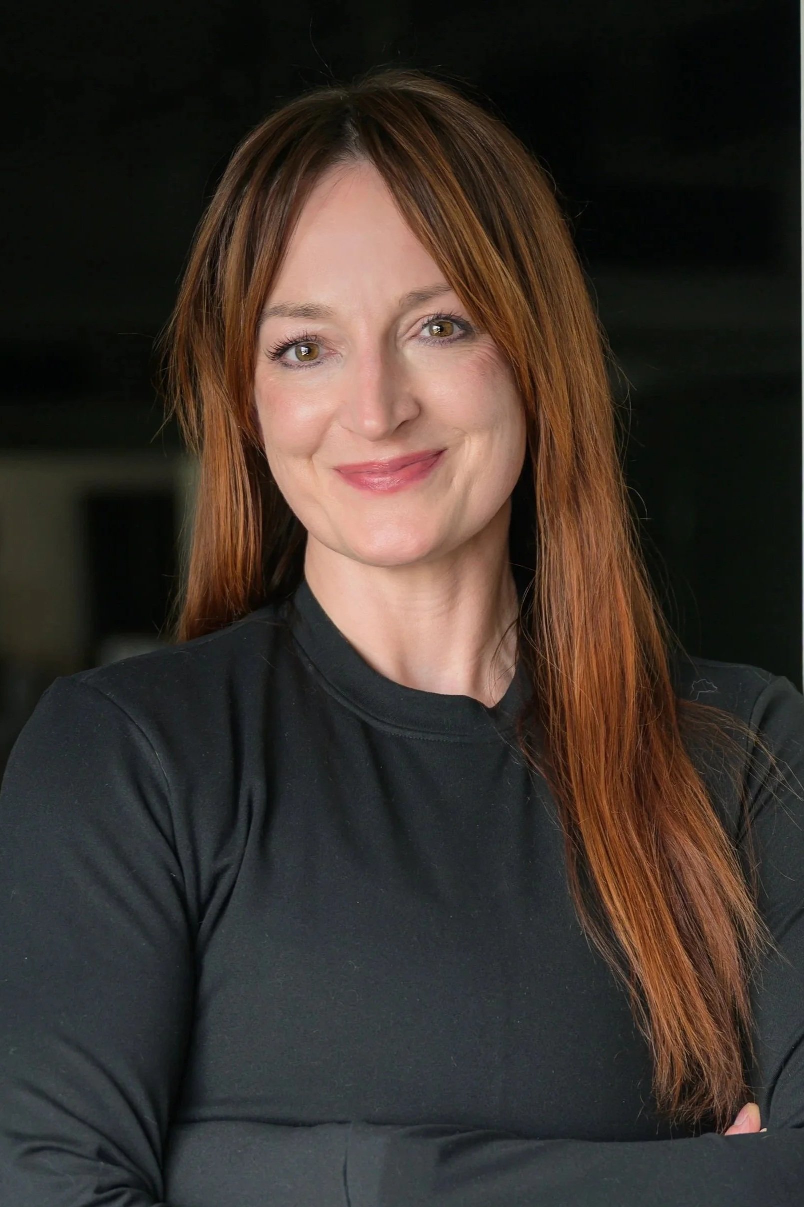 Black and white portrait of a smiling woman with long hair and tattoos on her arms, wearing a sleeveless top.