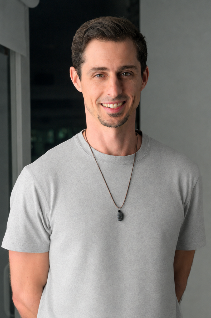 Black and white portrait of a smiling man with short hair wearing a dark shirt and necklace.