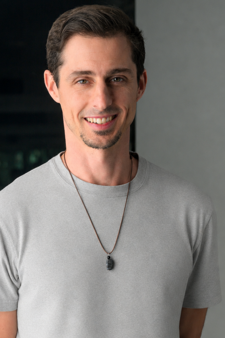 Black and white portrait of a smiling man with short hair wearing a dark shirt and necklace.