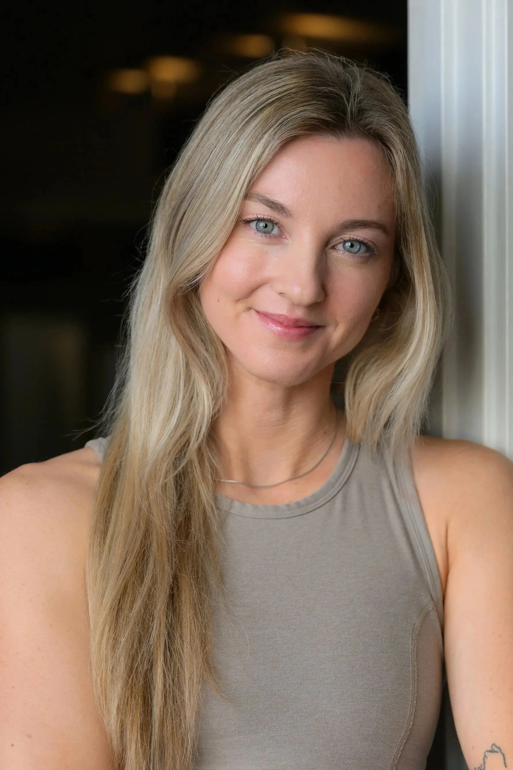 Black and white photo of a smiling person with long wavy hair wearing a tank top.