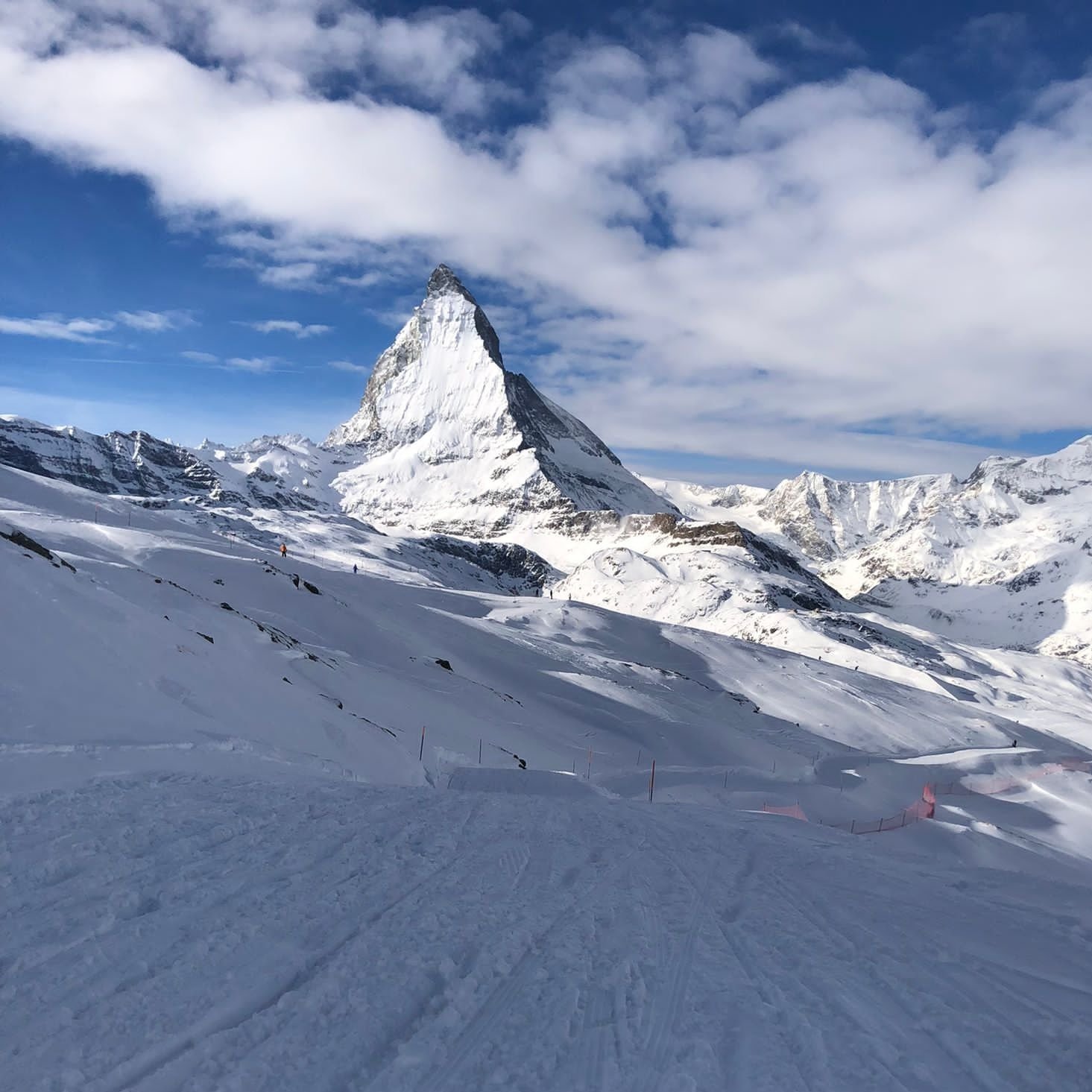 Snow-covered mountain landscape with a prominent peak, under a partly cloudy blue sky.