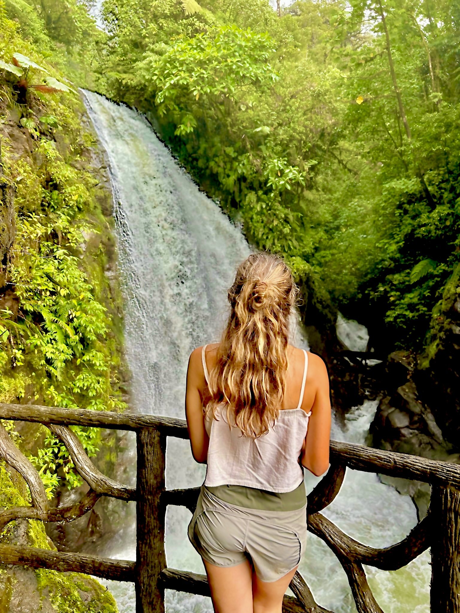 Woman admiring a waterfall surrounded by lush greenery.