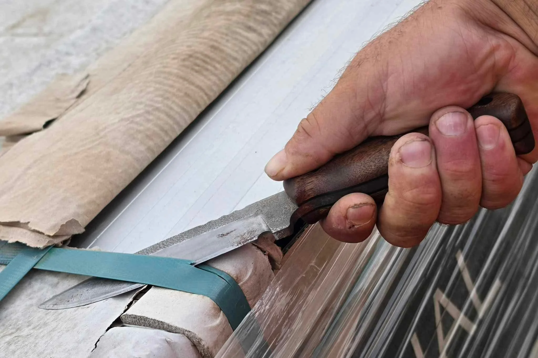 Close-up of a person's hands holding a knife, cutting a piece of banding strip in the field.