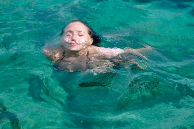 Une femme nageant dans l'eau turquoise, souriante et détendue.
