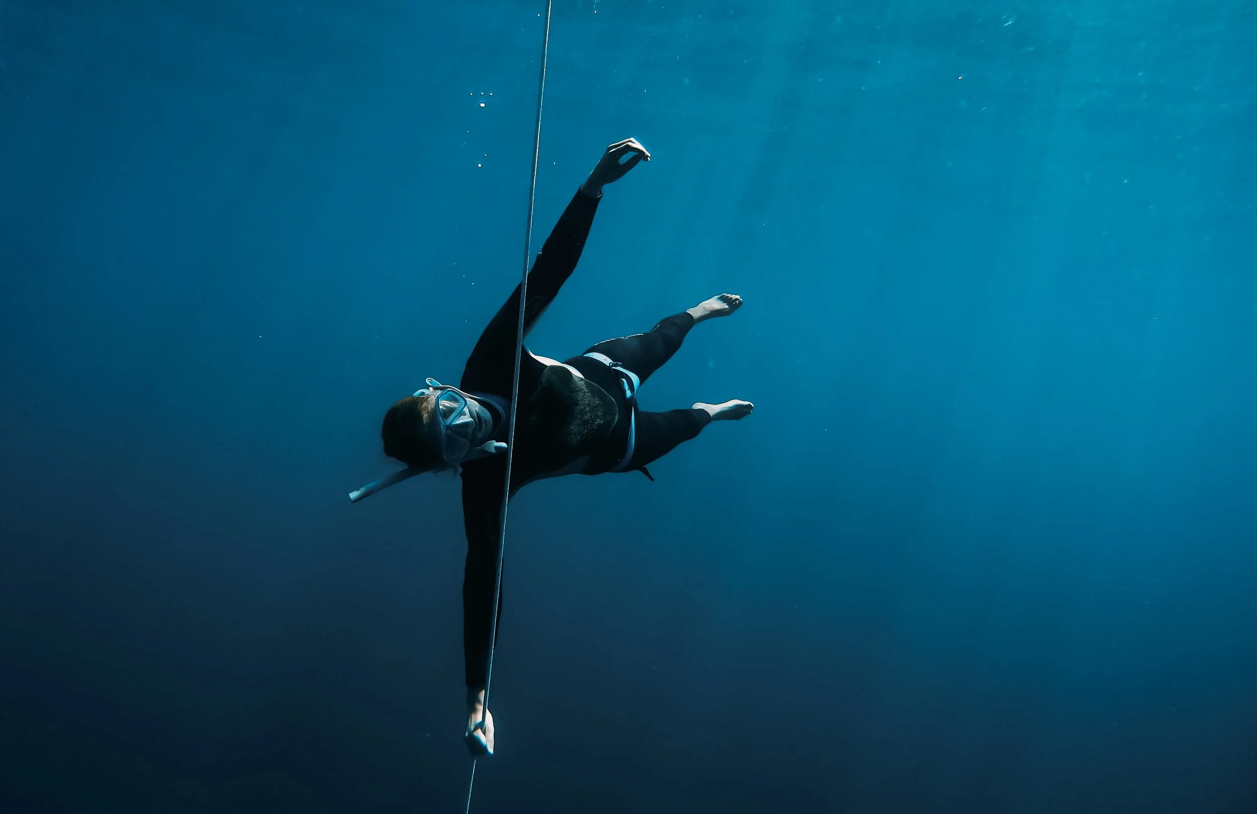 Une personne nage sous l'eau avec un masque de plongée et un tuba, portant une combinaison de plongée noire, en équilibre avec une planche de surf ou un tout autre objet plat.