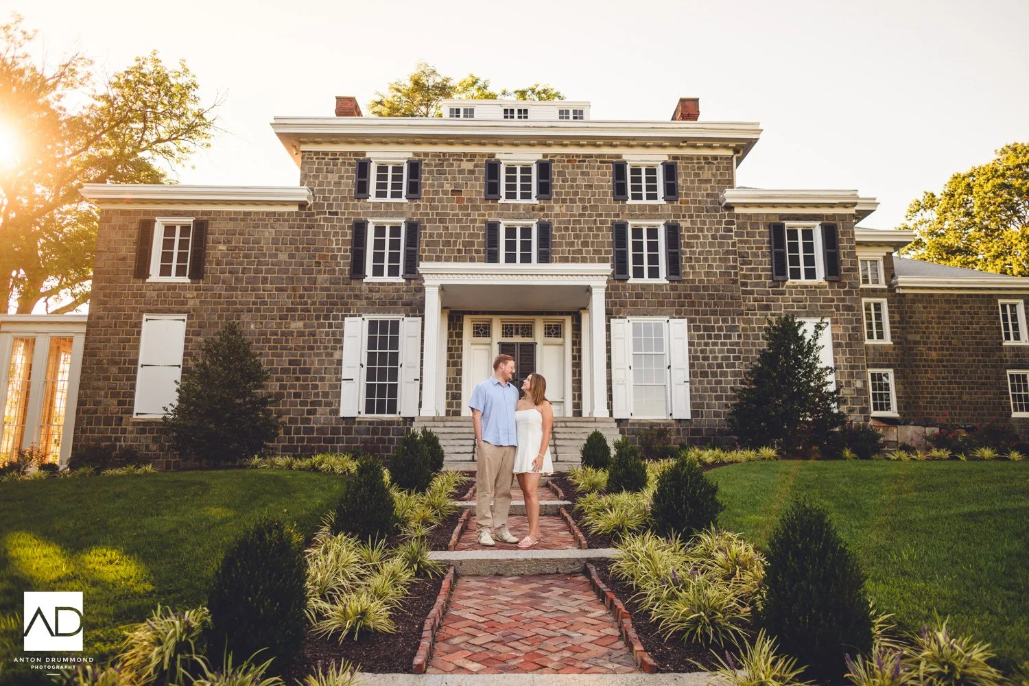 Couple on brick path before Gibraltar stone estate in golden afternoon light — Marian Coffin Gardens engagement session