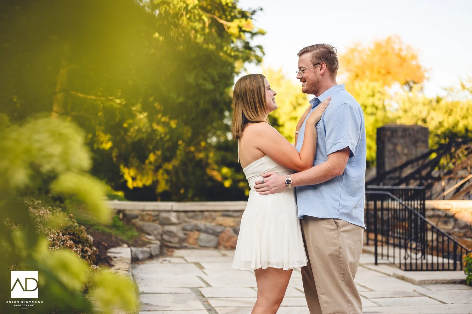 Romantic embrace on stone terrace with iron railing — New Castle County wedding photographer — golden trees behind