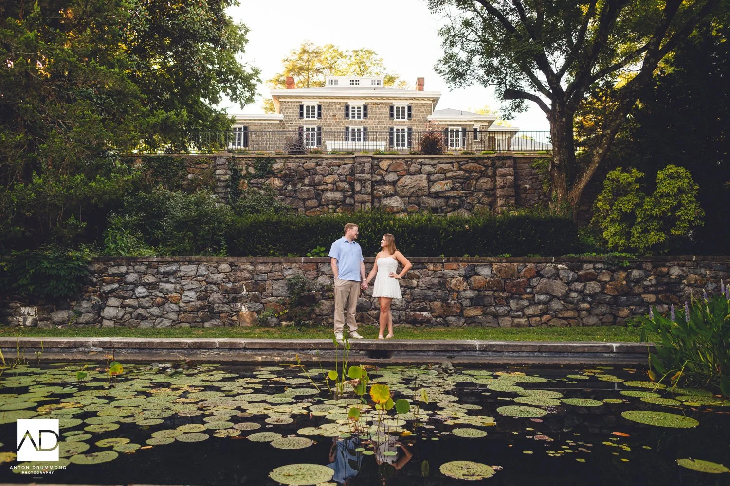 Wide view of lily pond covered in lily pads, couple on grassy bank above — Marian Coffin Gardens engagement session