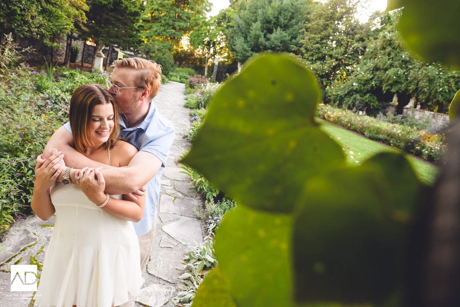 Summer garden path at Gibraltar — New Castle County wedding photographer — man hugging partner from behind as she laughs