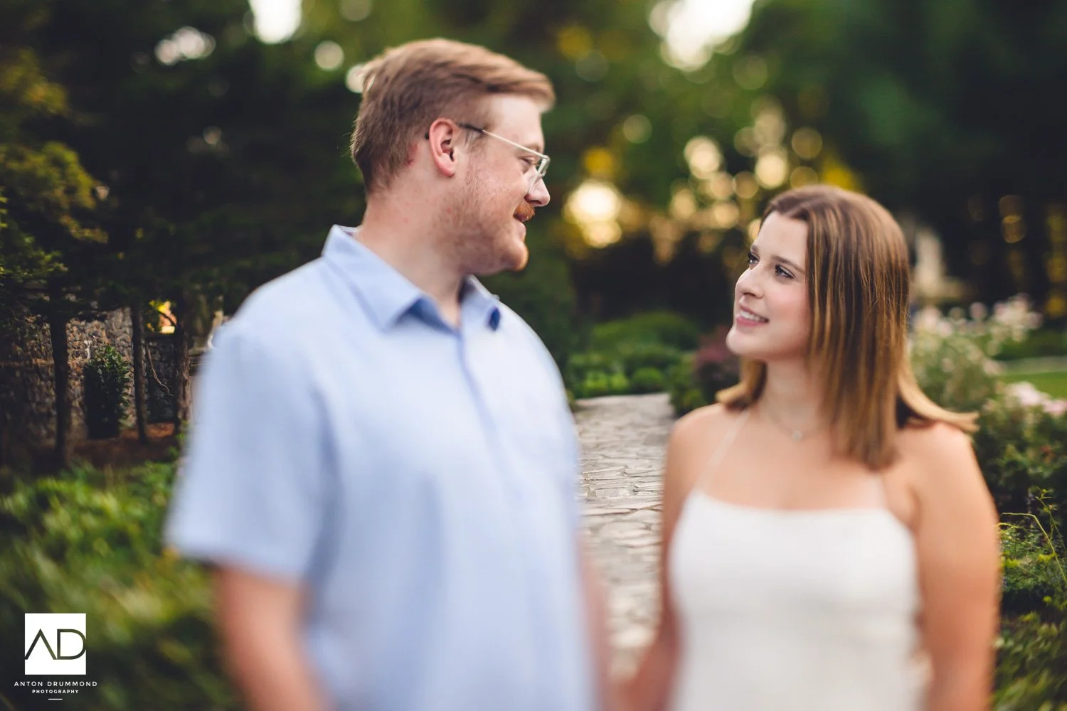 Wilmington DE engagement photographer captures couple gazing softly at each other in golden garden light