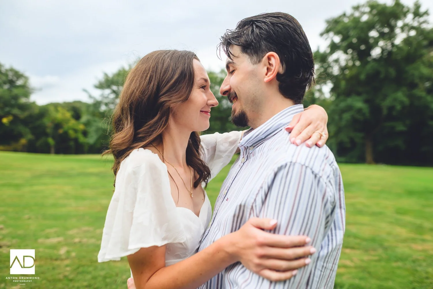 Emily and Joe nearly nose to nose on the open lawn, her hand resting on his shoulder — Wyncote PA engagement photographer