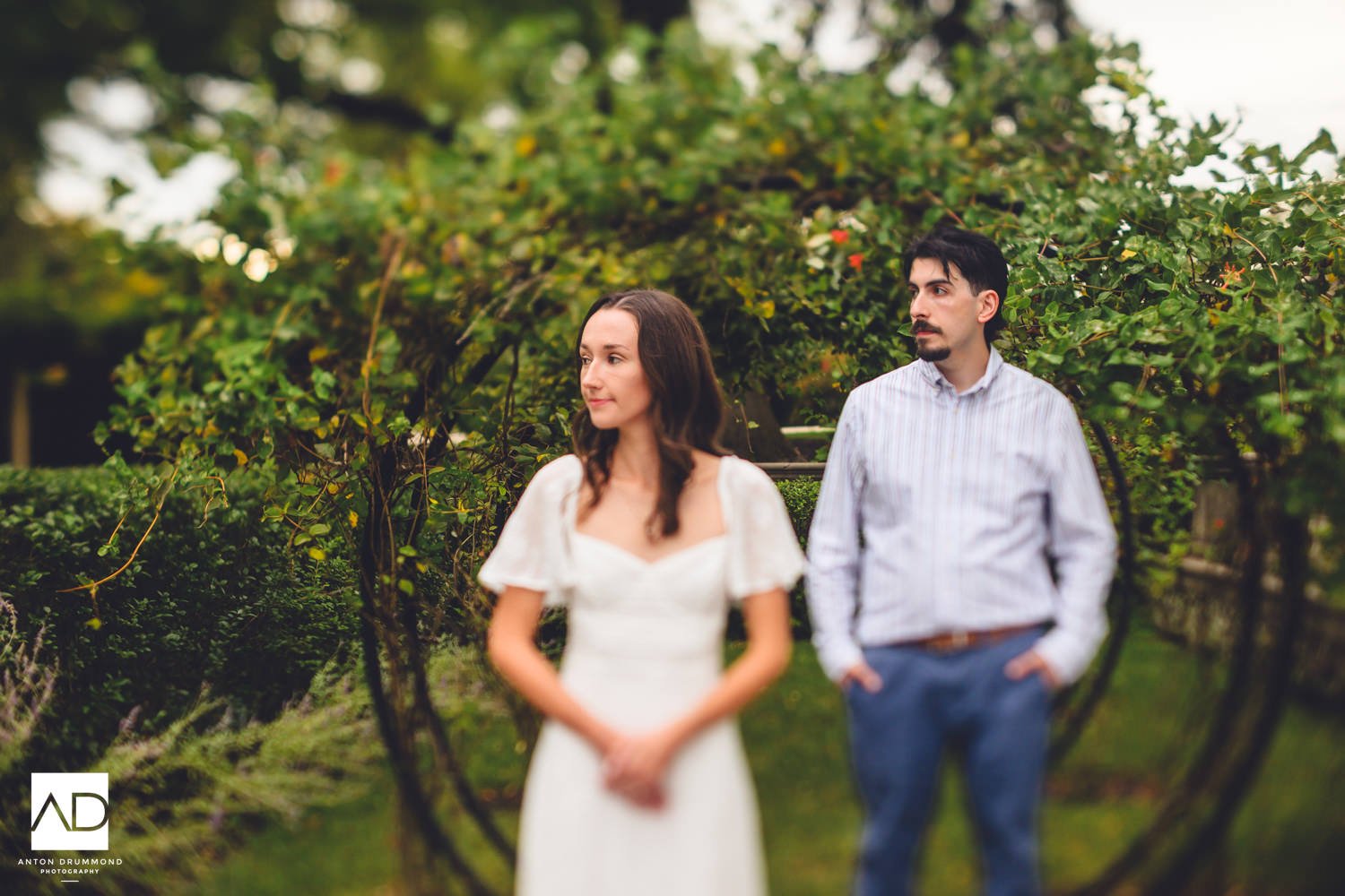 	Emily gazing into the distance, Joe watching her from behind the vine arbors — Montgomery County wedding photographer