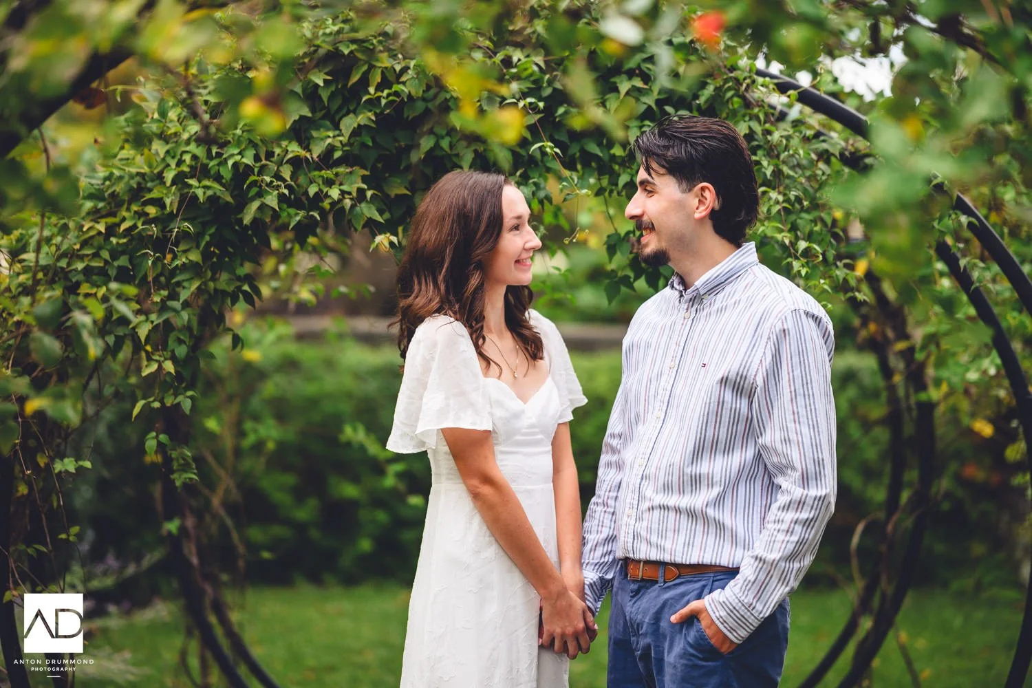 Couple laughing together inside the circular vine arbors, stone balustrade to the right — Curtis Arboretum engagement session
