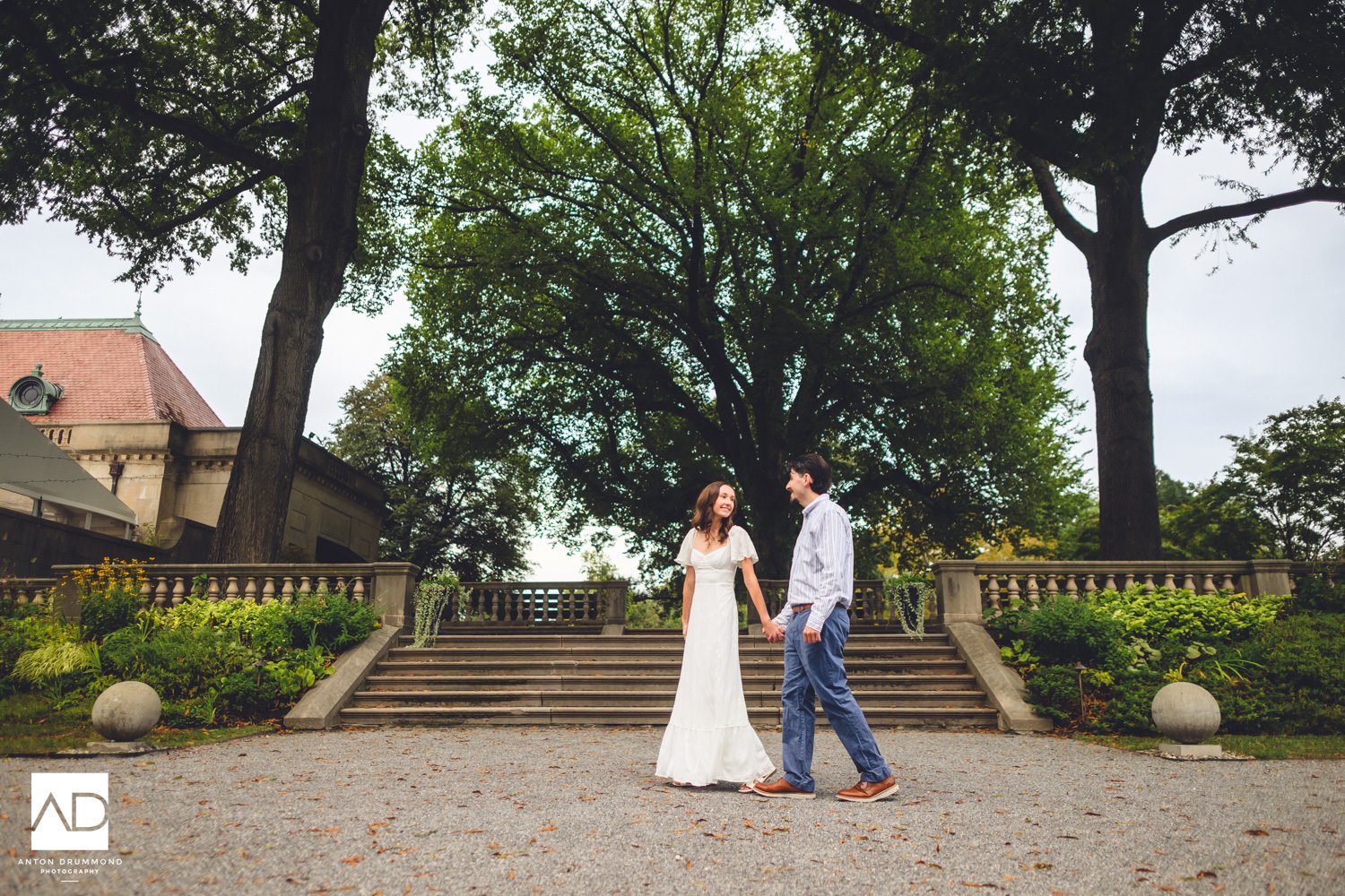 	Emily and Joe walking hand in hand on the gravel courtyard, stone spheres flanking — Montgomery County engagement photographer