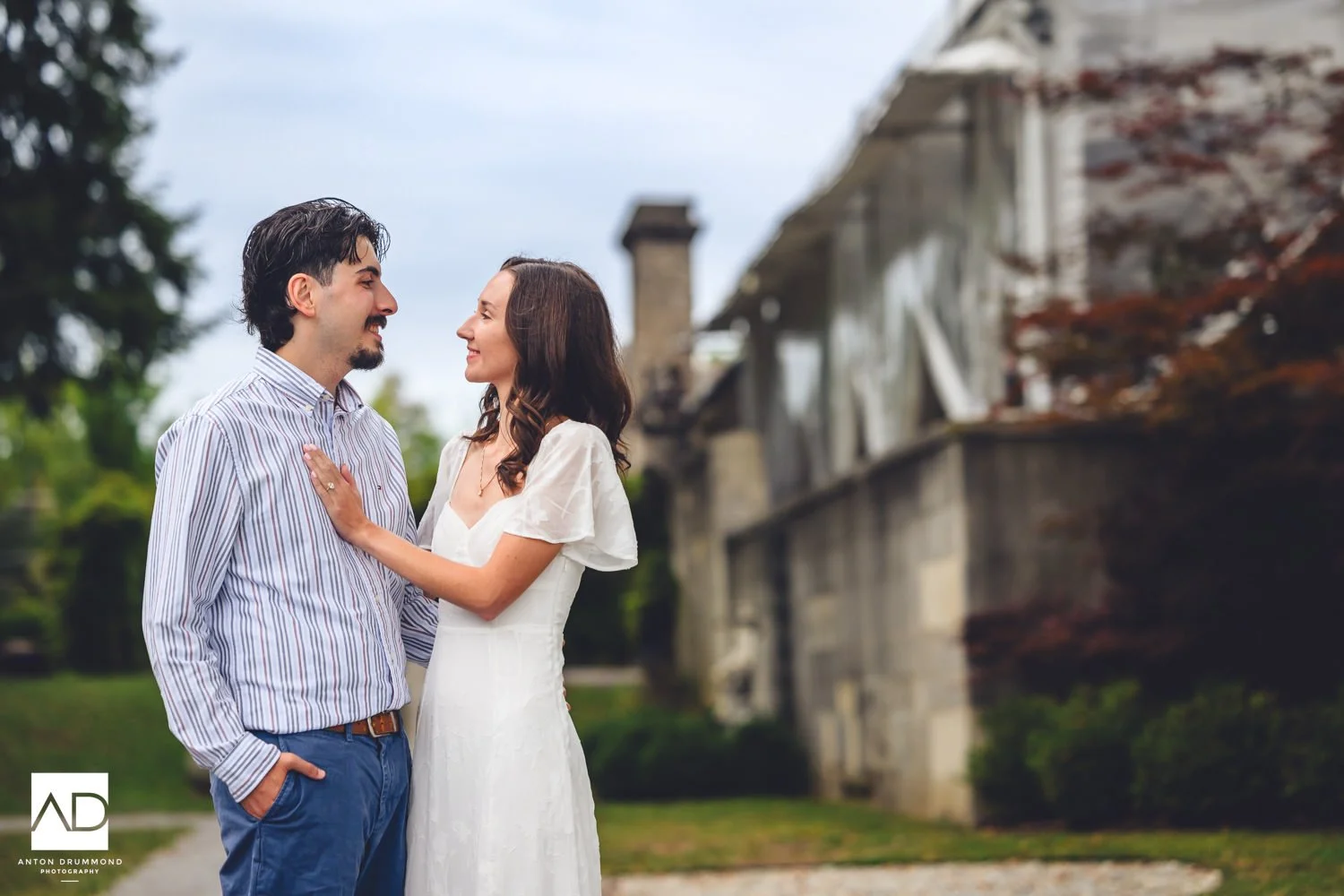 	Emily and Joe sharing a quiet smile, red ivy climbing the stone manor wall behind — Montgomery County wedding photographer