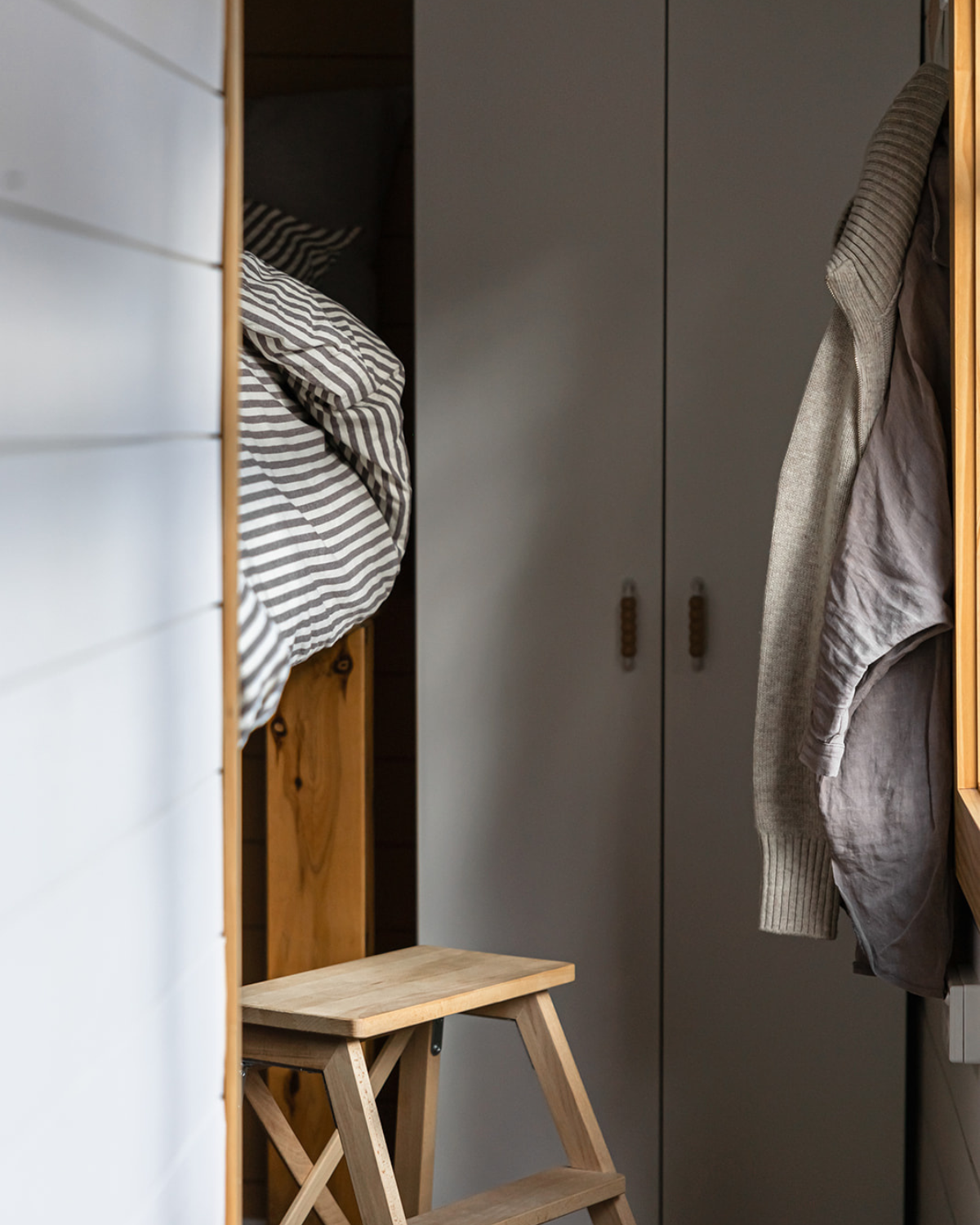 Built-in wardrobe with striped linen bedding and wooden step stool inside the Moss & Wheels converted bus