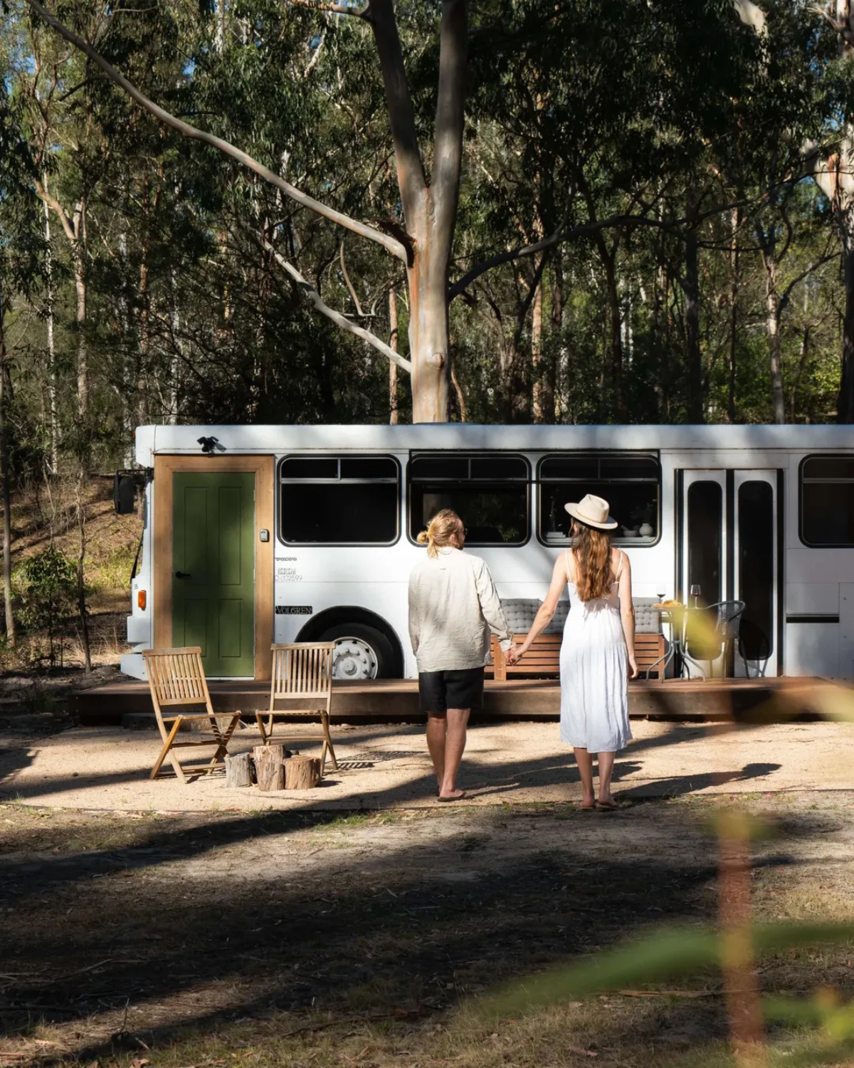 Couple holding hands walking towards the Moss & Wheels converted bus deck with outdoor seating and firepit