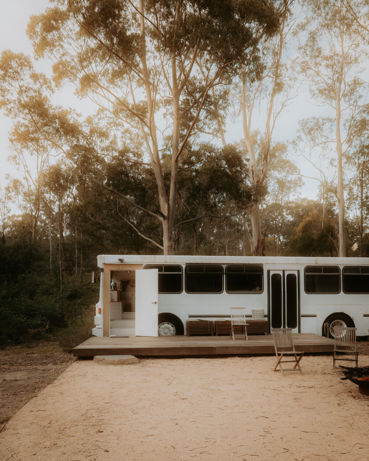 White converted bus accommodation with timber deck surrounded by eucalyptus trees at Moss and Wheels, Cottles Bridge Victoria