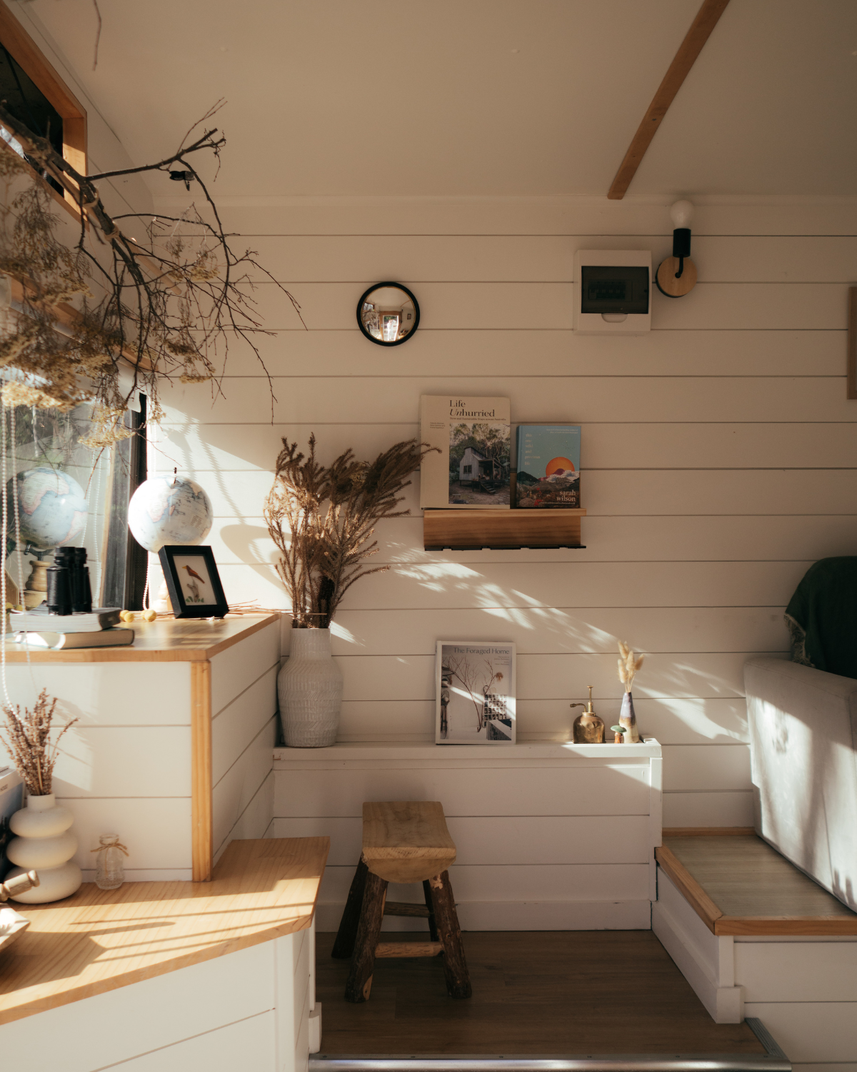 Warm sunlit interior of the Moss & Wheels converted bus with dried botanicals, globe, books and white shiplap walls