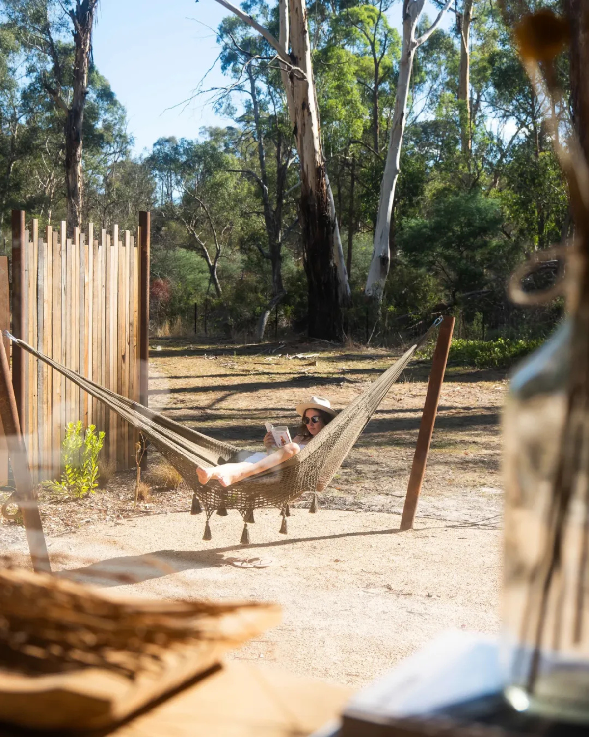 Woman relaxing in a hammock reading a book at Moss & Wheels converted bus stay surrounded by Australian bushland