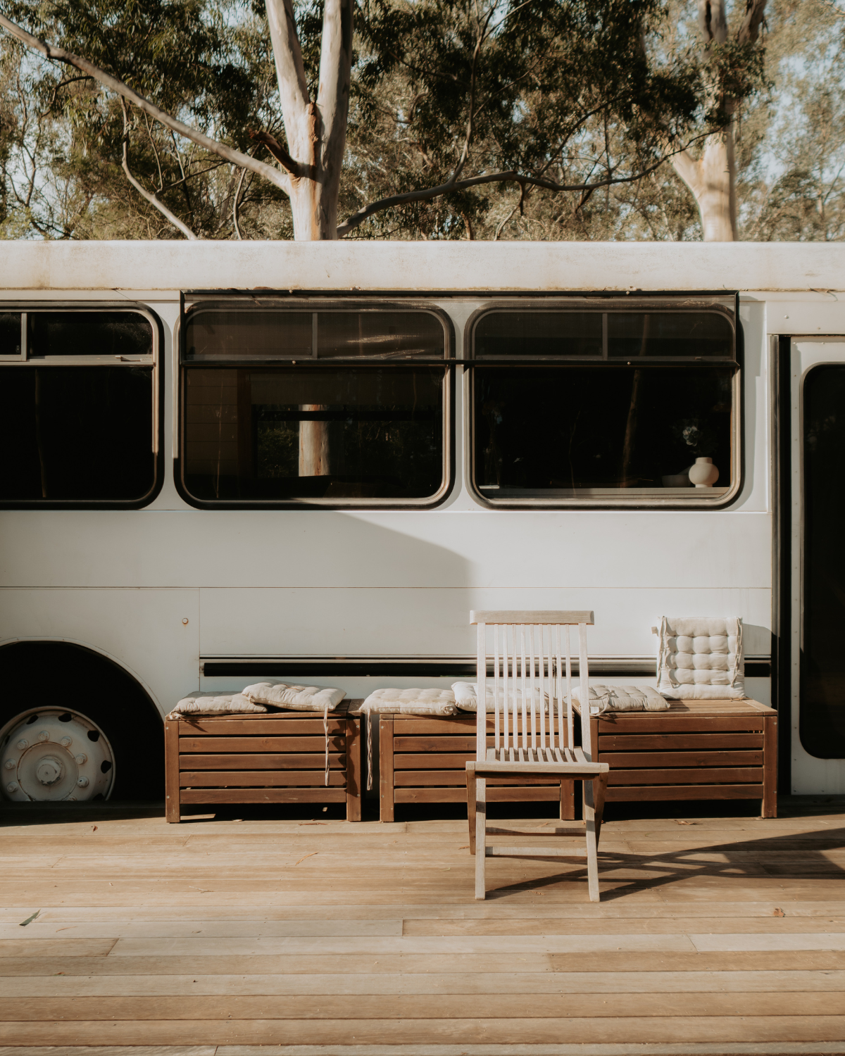 Timber deck with wooden bench seats and cushions alongside the Moss & Wheels converted bus exterior at golden hour