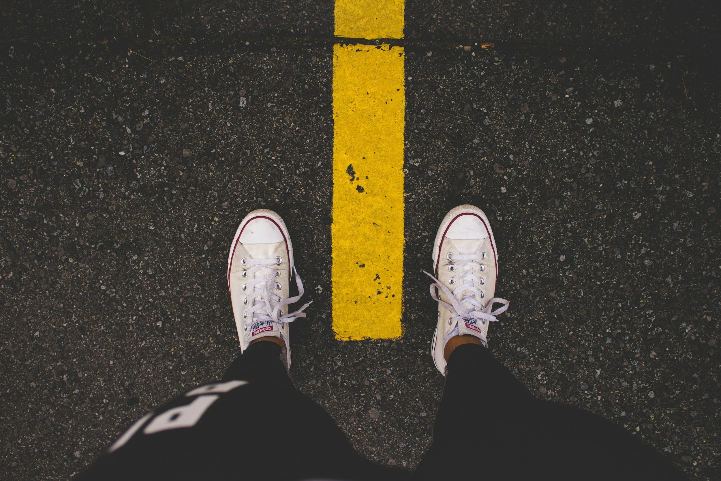 feet in sneakers standing over a yellow line on the road image