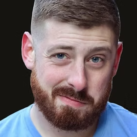 A man with short brown hair and a beard, wearing a blue shirt, winking and looking at the camera.