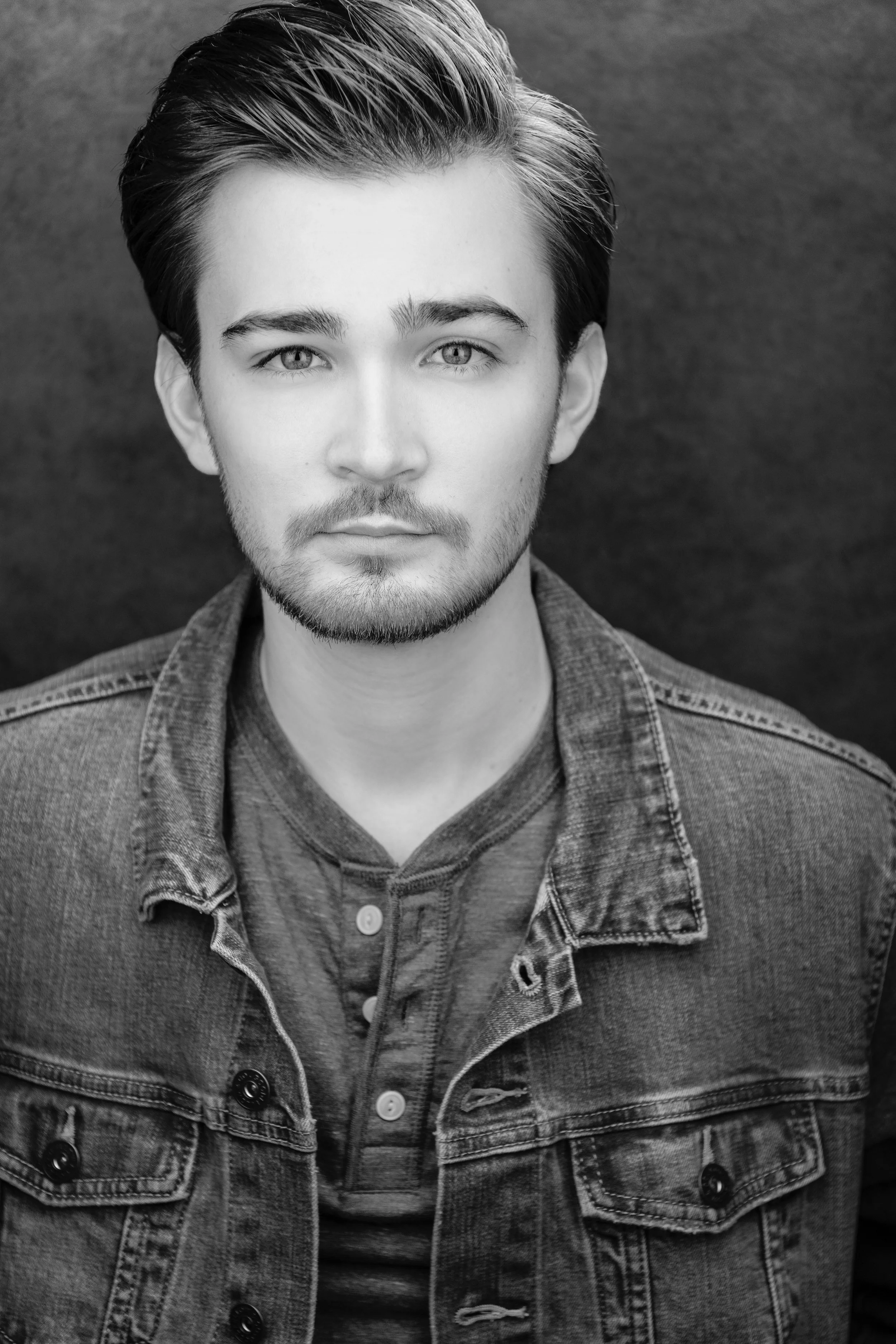 Black and white portrait of Giacomo with short, styled hair, facial hair, and light-colored eyes, wearing a denim jacket and a button-up shirt.
