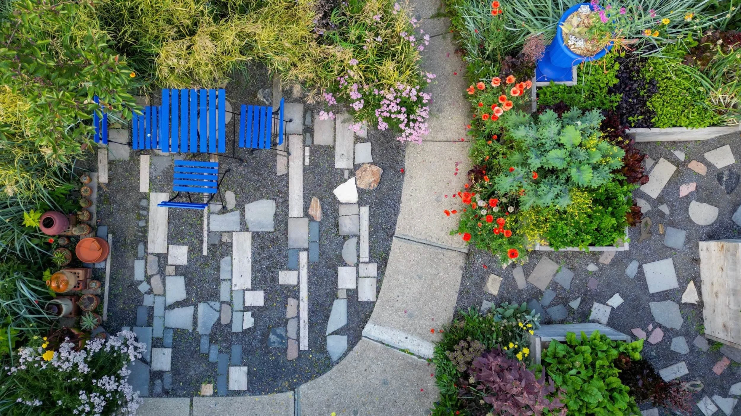 Plan view photograph of a patio with a blue bistro set, curved path, and dense planting beds showing texture and colour