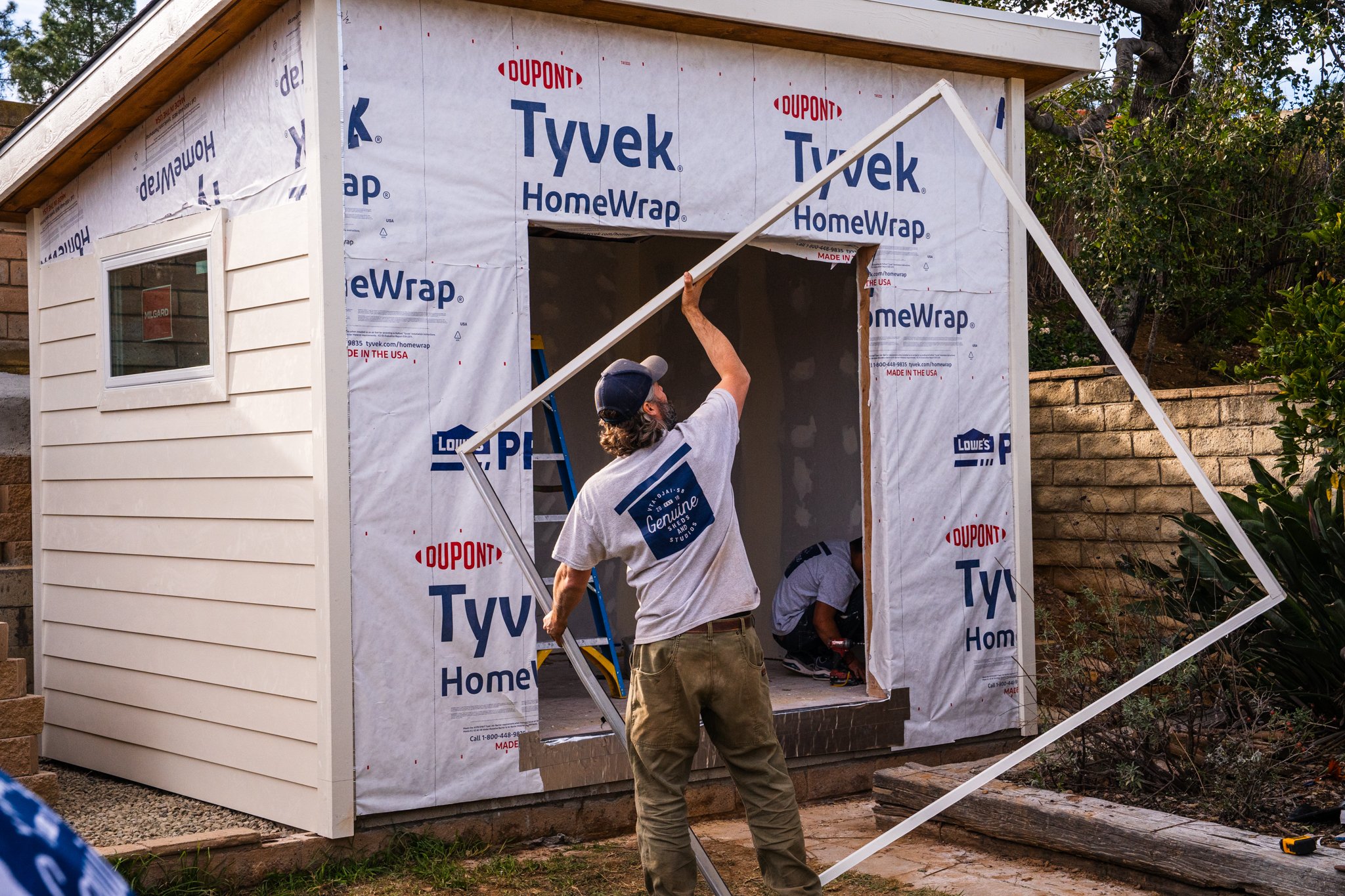 Workers installing a door frame on a small building with Tyvek HomeWrap. Genuine Sheds and Studios
