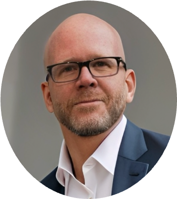 A middle-aged man with a bald head, wearing glasses, a white shirt, and a dark blue blazer.