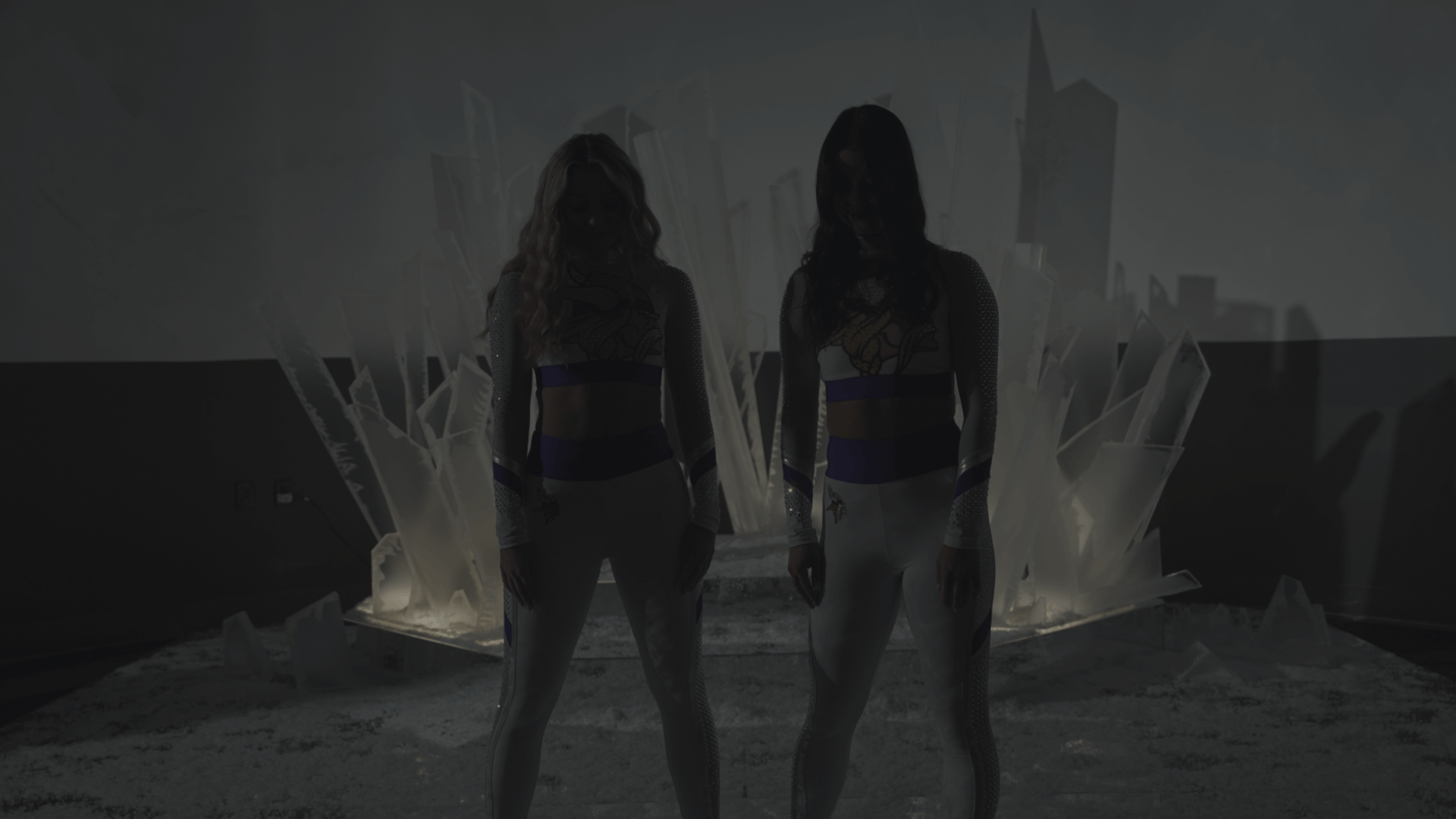 Two silhouetted figures in athletic wear stand in front of an abstract ice-like backdrop made of translucent geometric shapes.