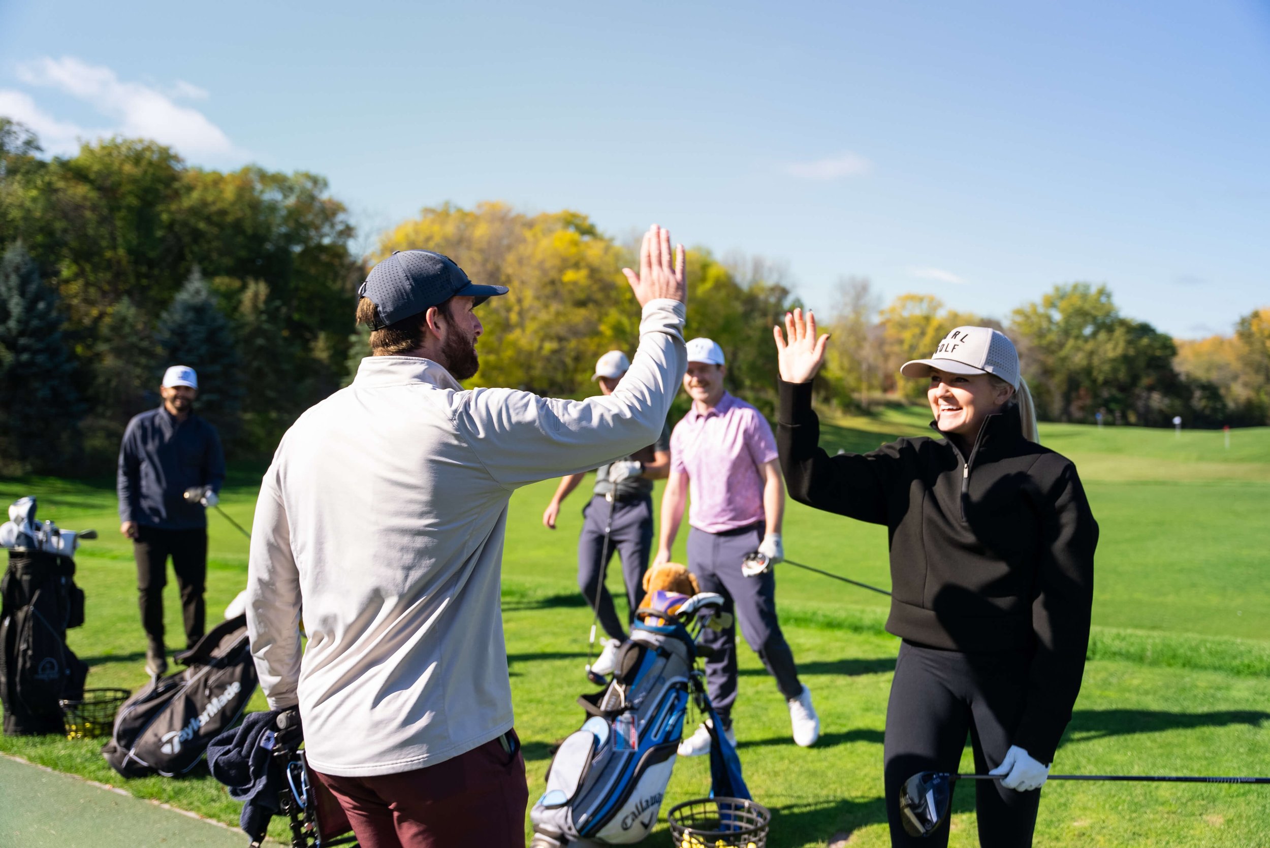 Group of people high-fiving on a golf course with clubs and bags.