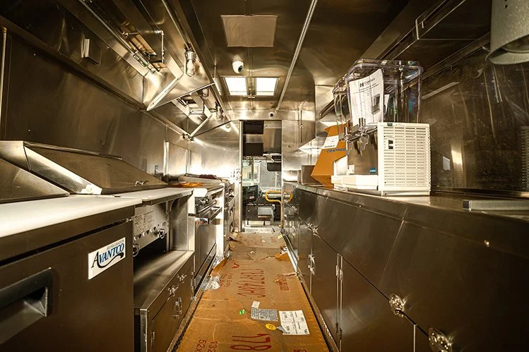 The interior of a commercial kitchen or food truck with stainless steel appliances, a cleaning cloth, and cardboard on the floor.