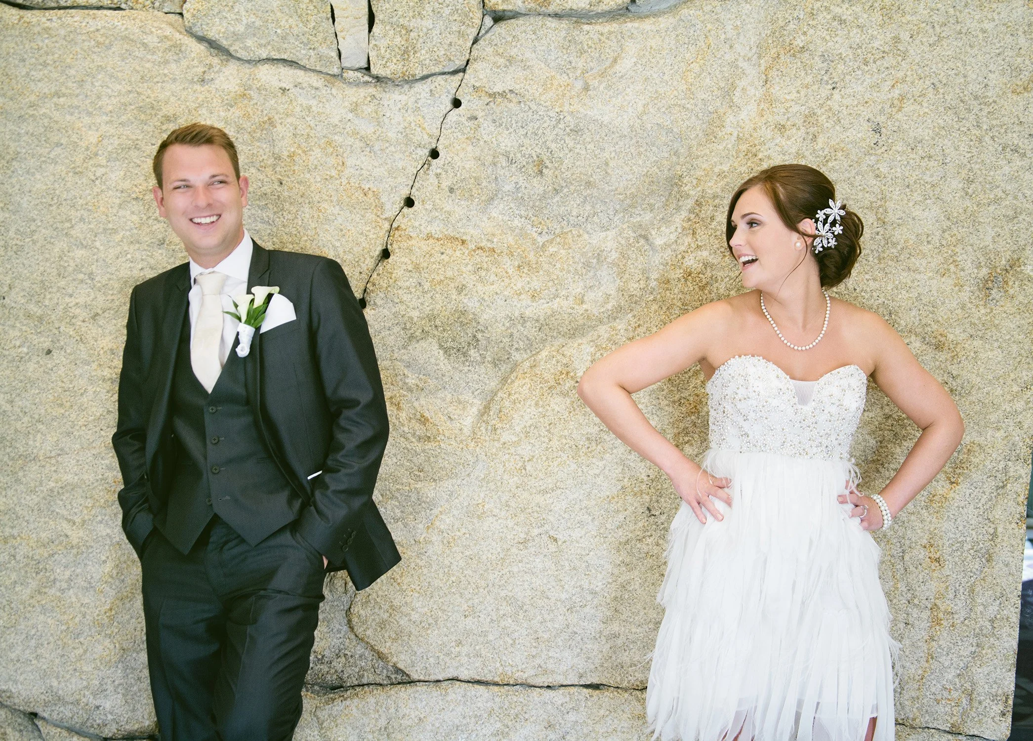 Bride and Groom standing in front of a stone wall, candidly laughing and looking at each other