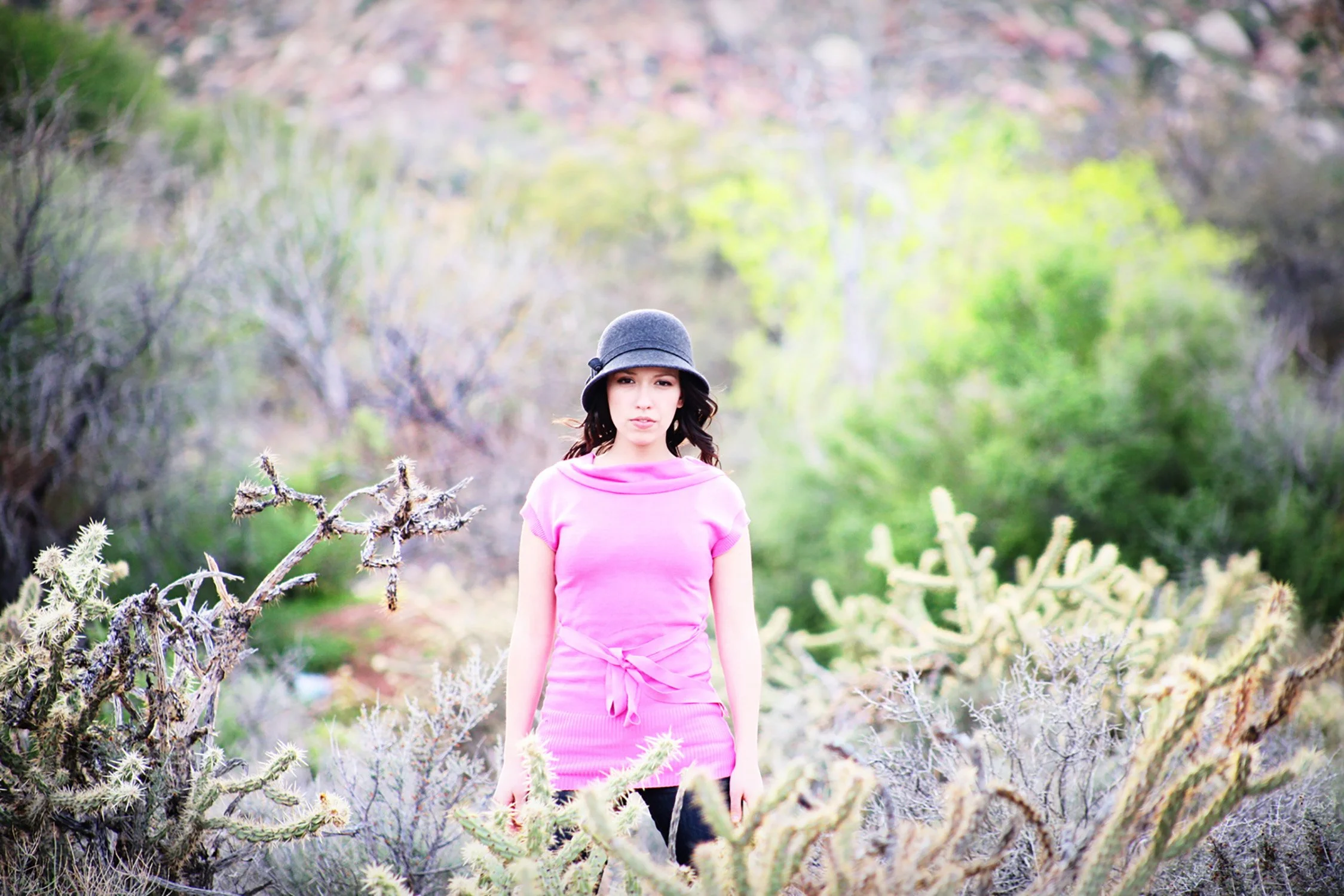 wearing a pink shirt, a high school senior stands out while surrounded in the desert with cactus and pushes around her
