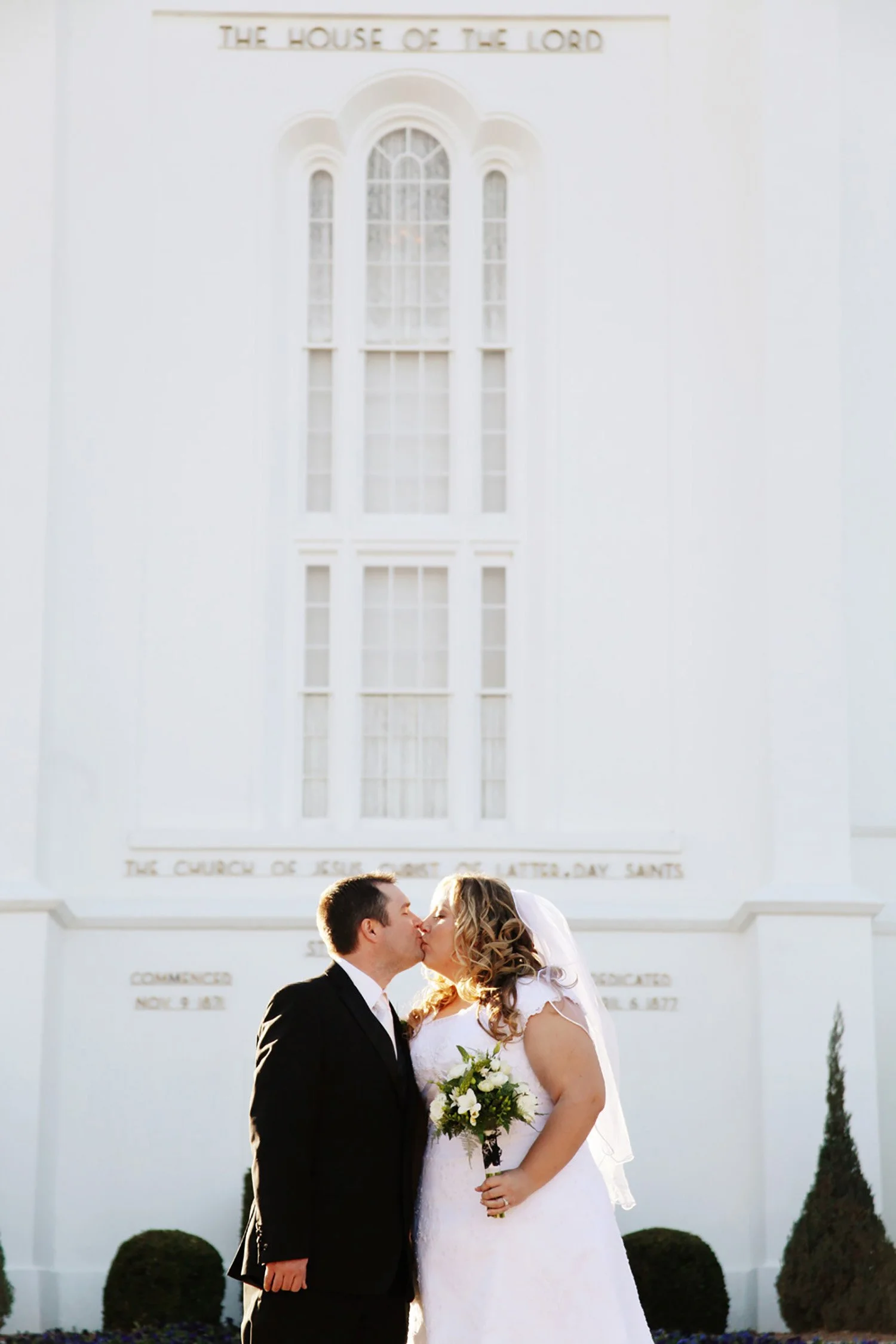 A couple in front of the St. George LDS Temple kissing with the light shining on them from off camera
