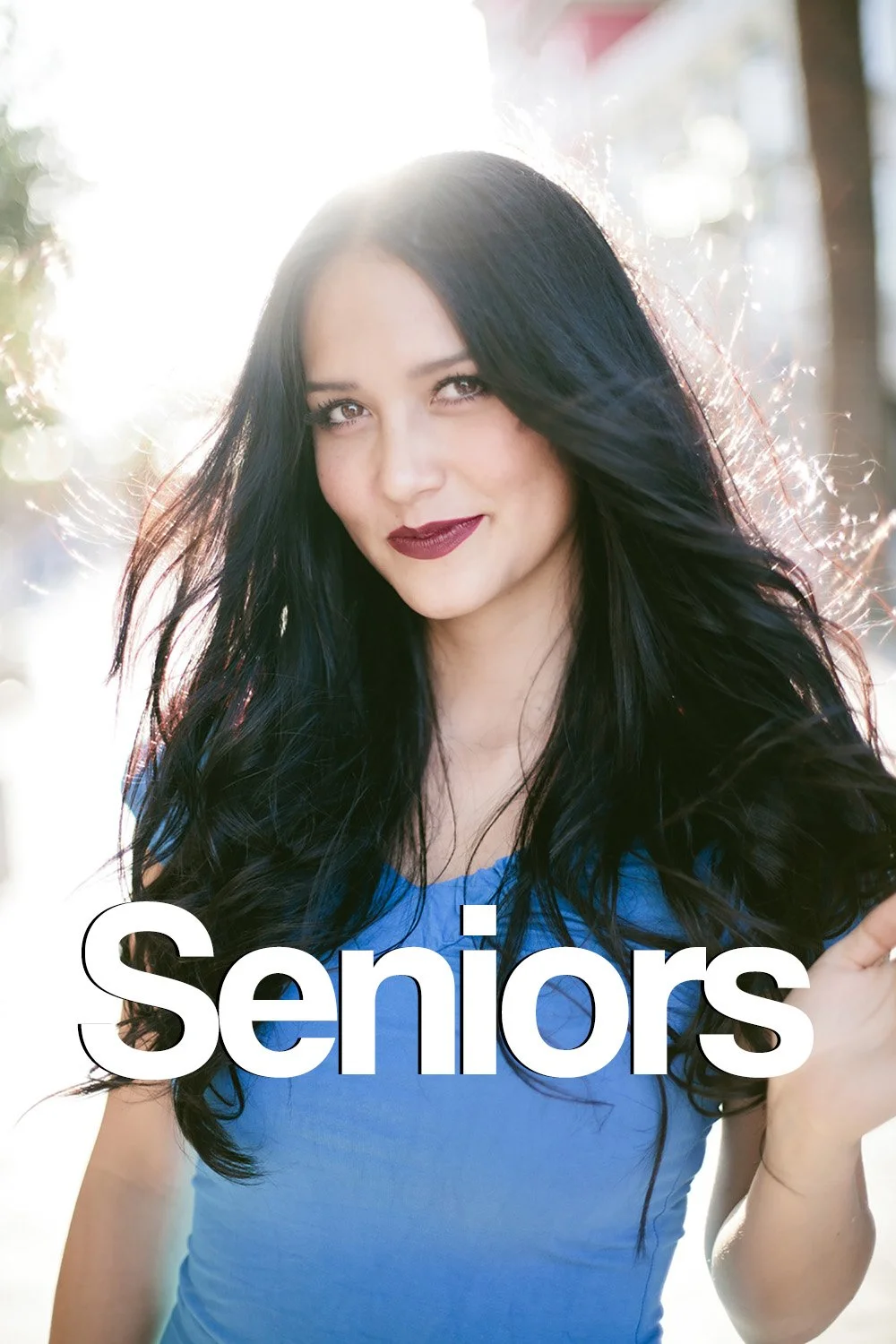 high school senior is smiling at the camera with the sun behind her and hair blowing in the wind at Tivoli Vilage