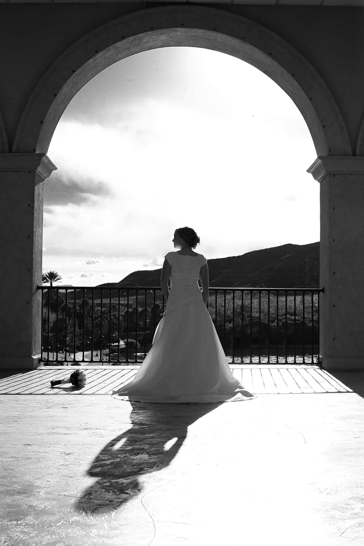 A black and white image of a bride standing in a front of an open frame bridge at Lake Las Vegas with her back to the camera