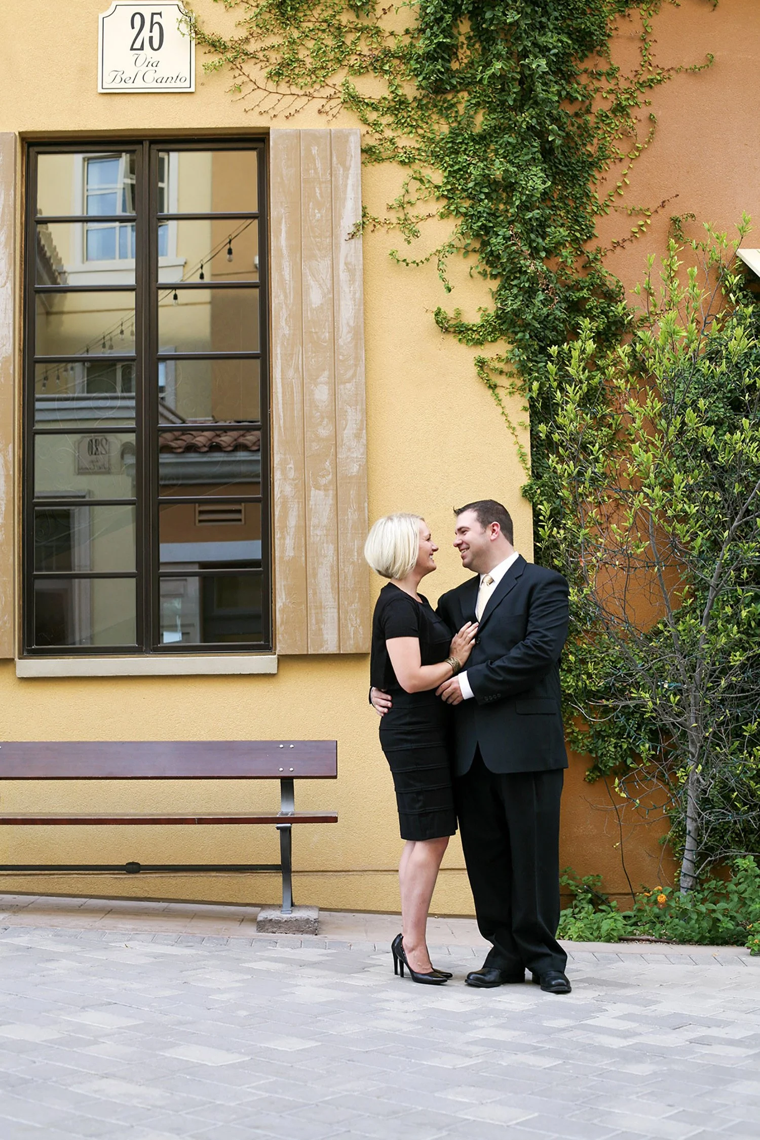 A engaged couple standing near an Italian inspired building holding each other and talking candidly