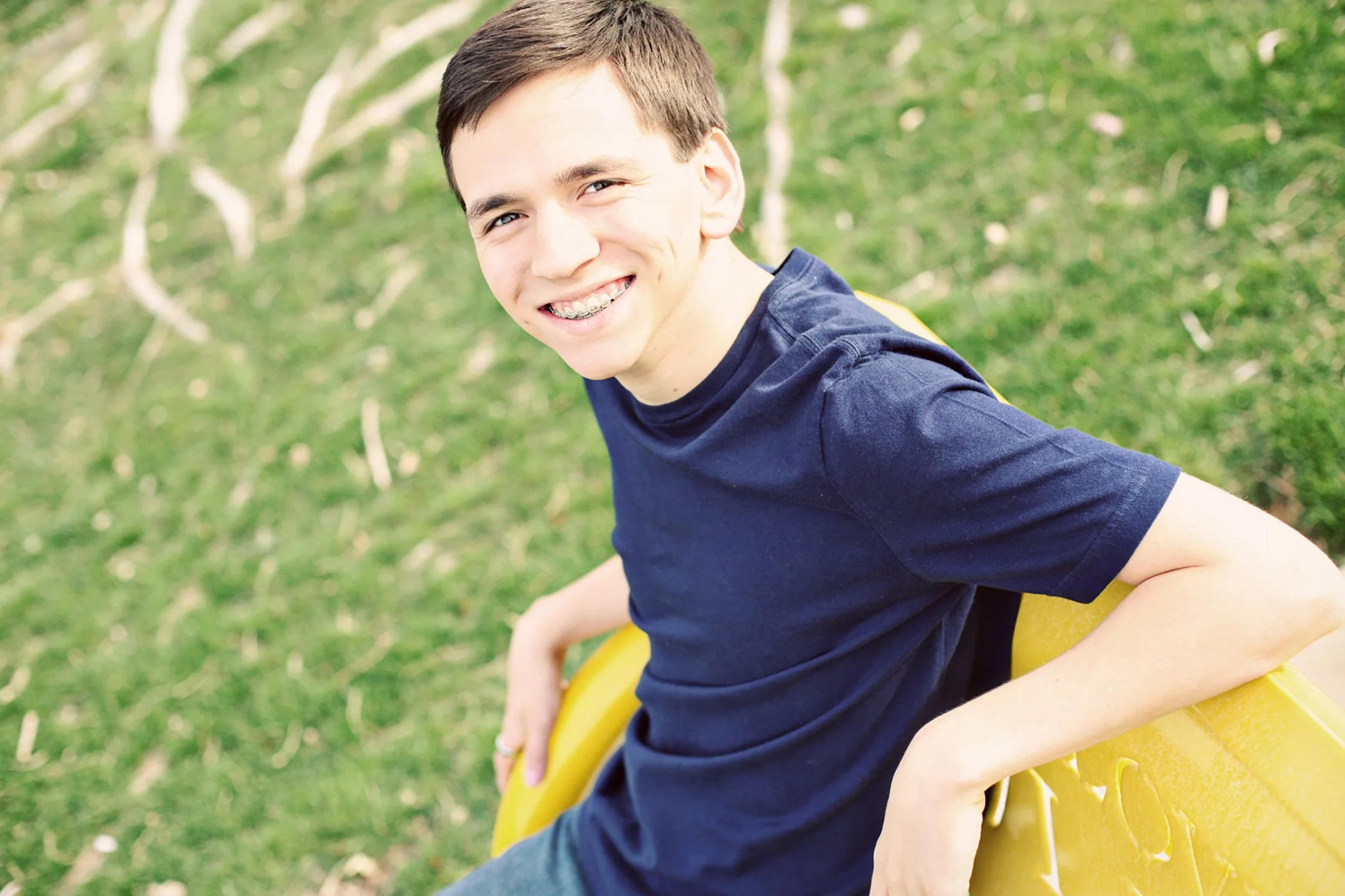 a high school senior is sitting on a bright yellow bench. He is smiling and looking at the camera.