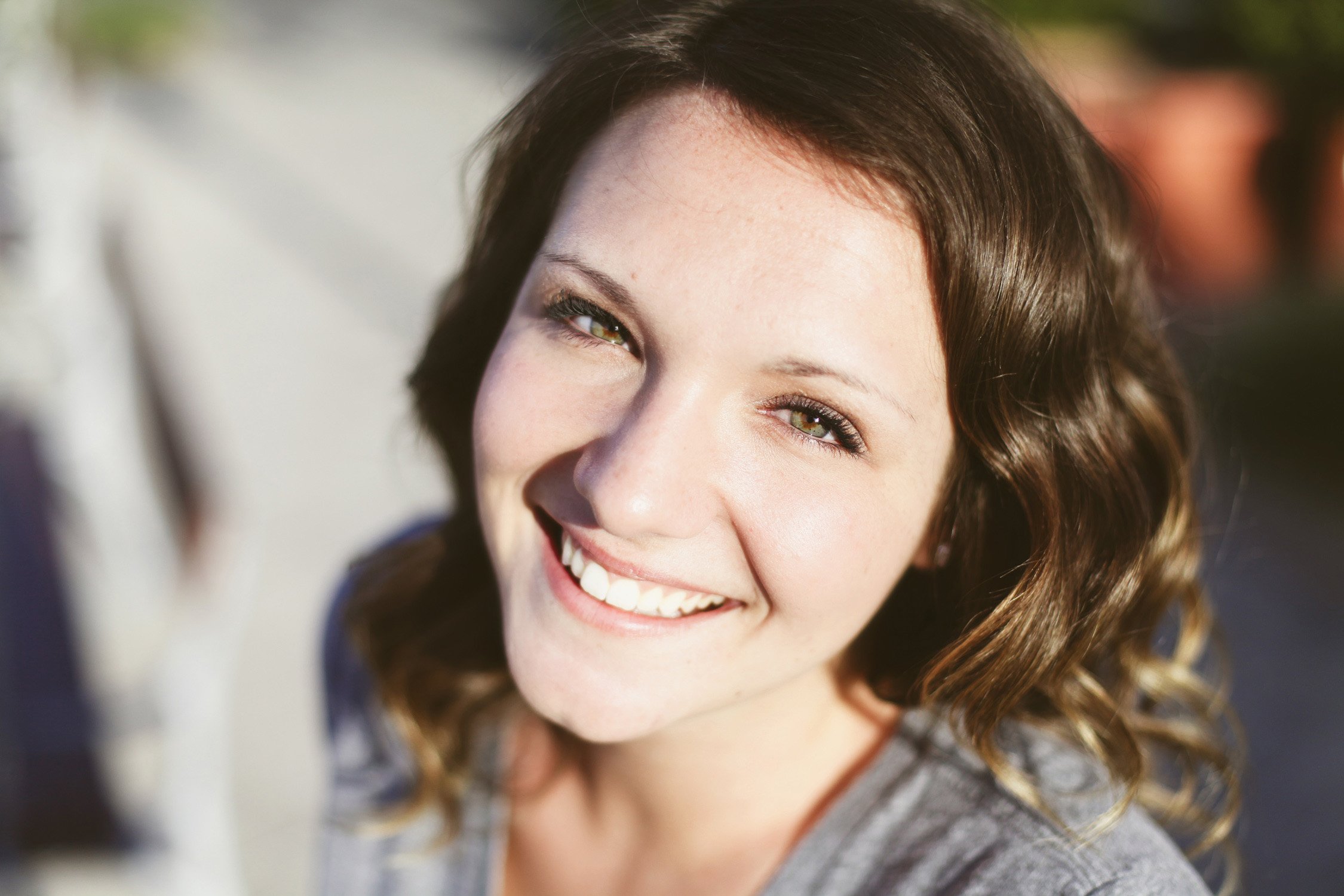 An up close image in a high school senior, she is smiling at the camera showing teeth and her bright green eyes.