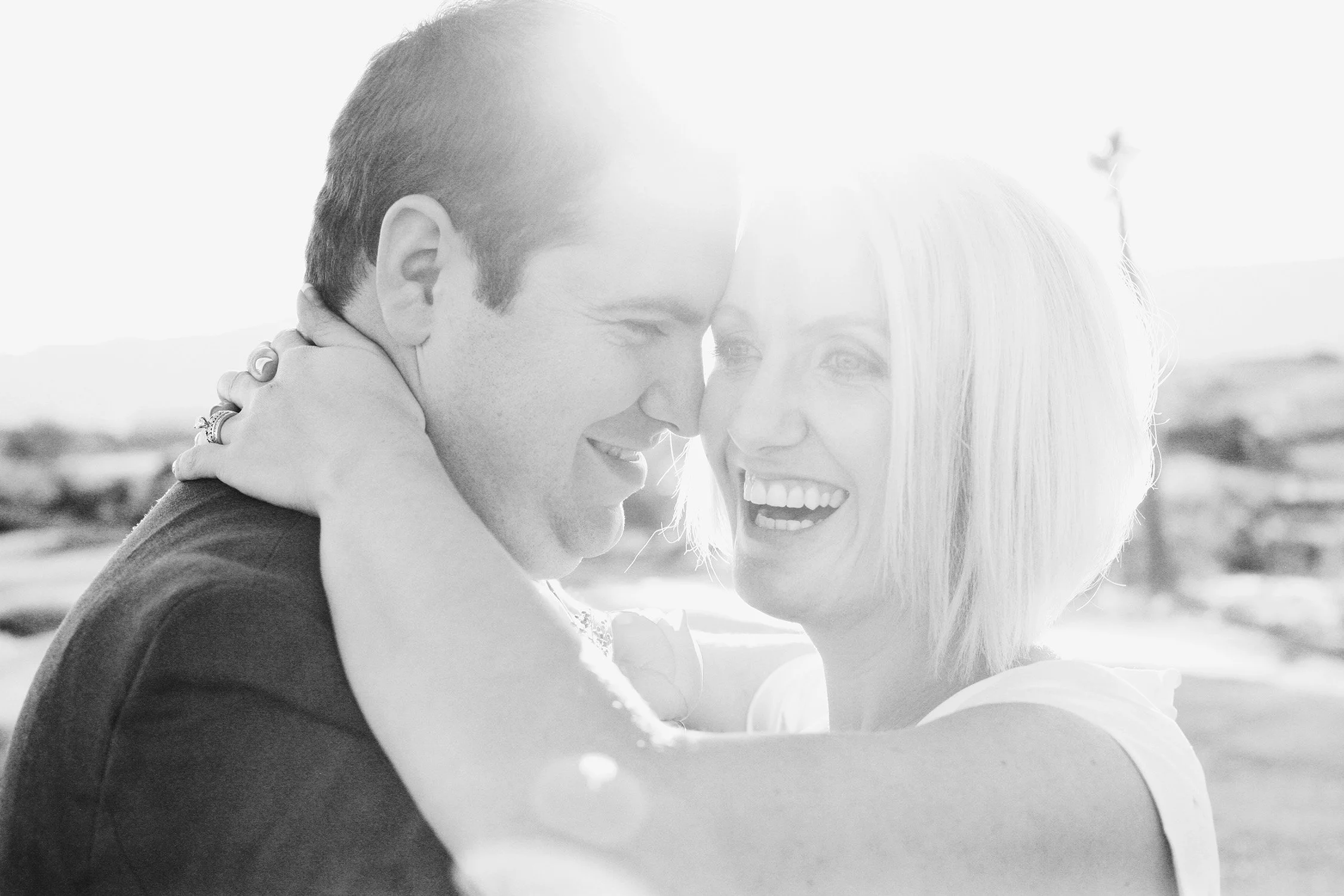Upclose of bride and groom holding each other close, foreheads touching, groom looking at bride smiling and bride laughing lookig off camera, photo in black and white