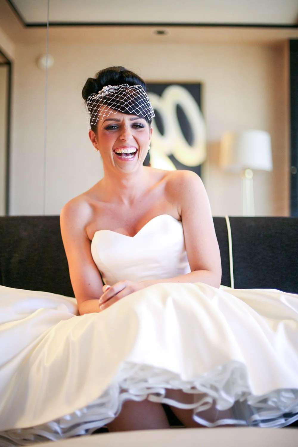 a bride sitting on a couch in the Wynn hotel room smiling and looking at the camera